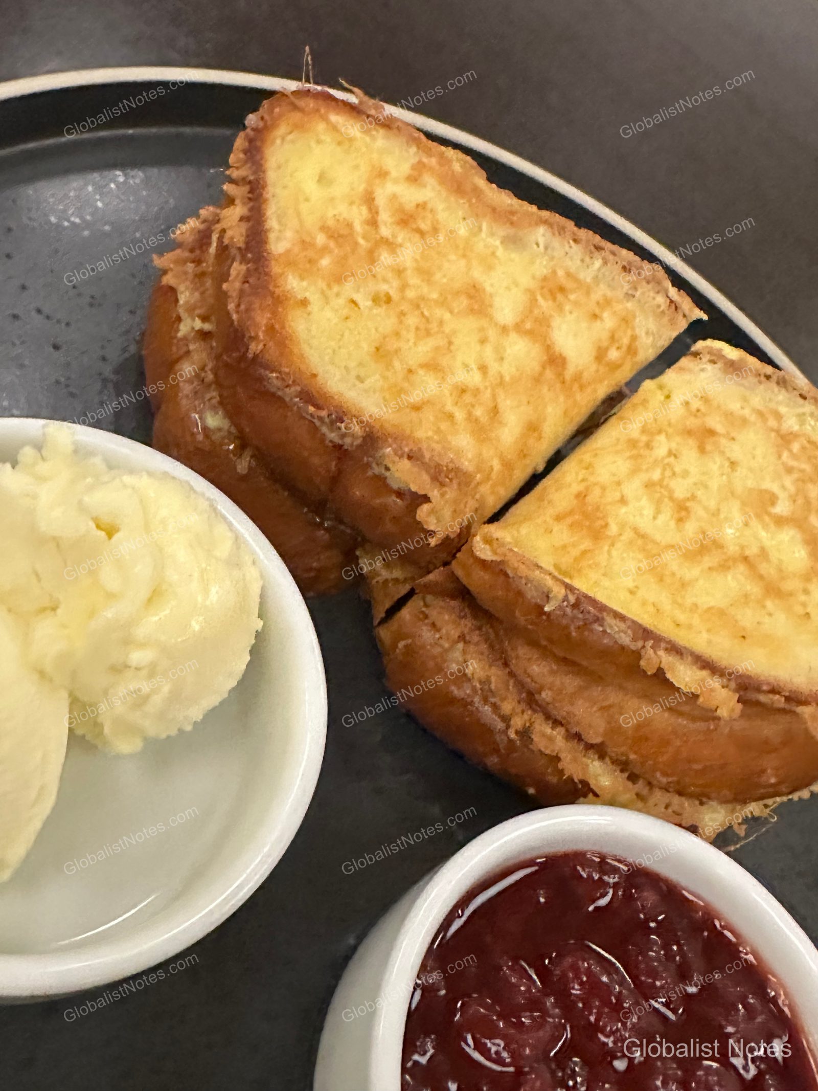Two slices of golden-brown French toast served on a black plate at Hyatt Regency Los Angeles International Airport, accompanied by a small dish of butter and red berry compote.