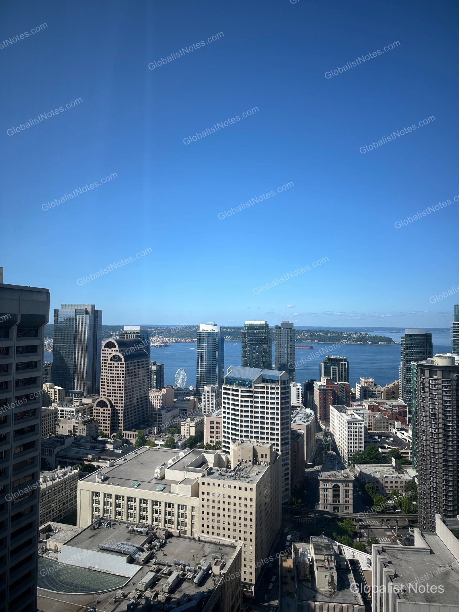 View of downtown Seattle from a guest room at Hyatt Regency Seattle, showing the dense city skyline, the blue waters of Elliott Bay, and the distant Ferris wheel on a clear day.