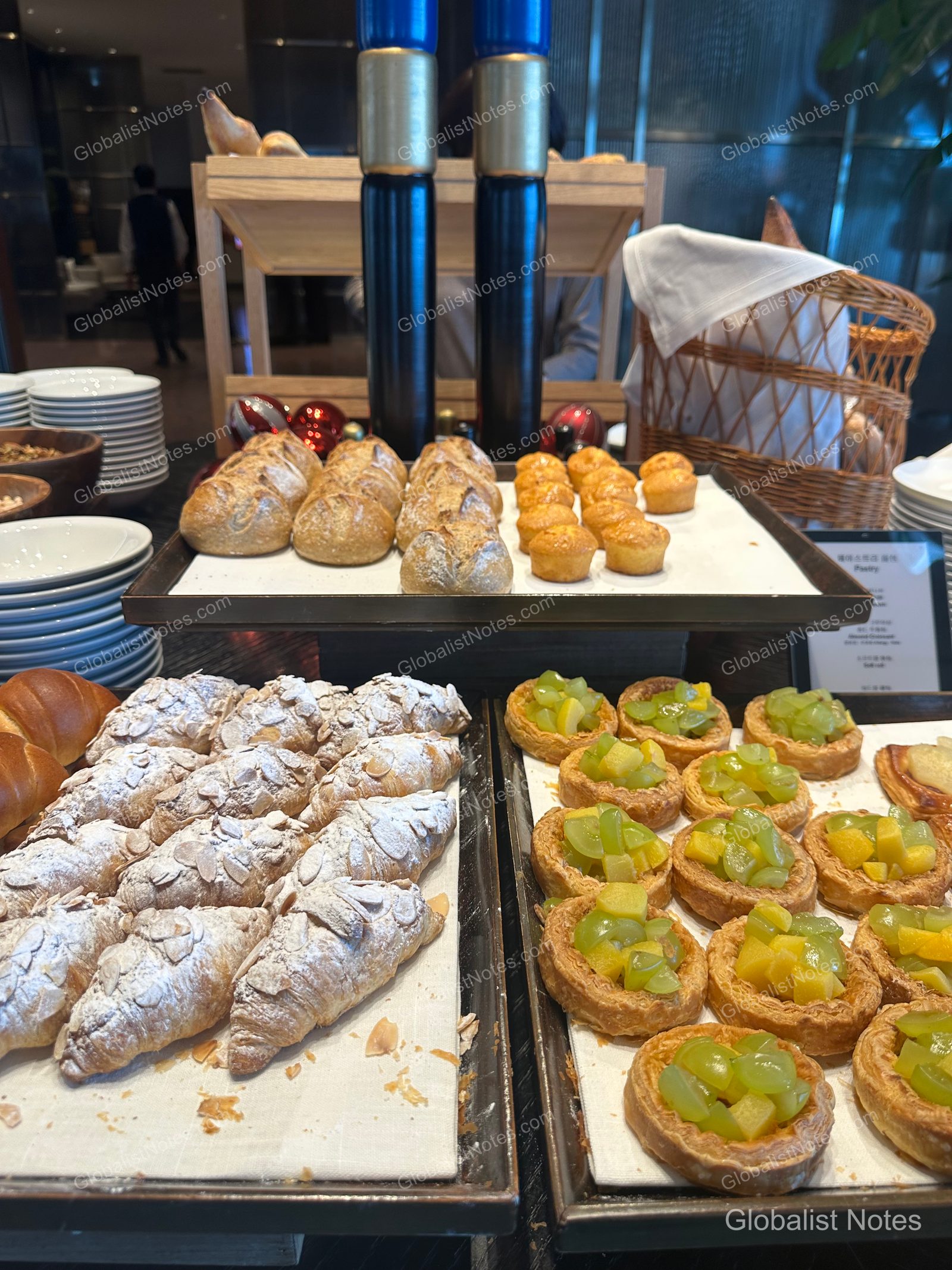Bakery station at the Grand Hyatt Jeju breakfast buffet, featuring trays of almond-topped croissants, fruit-topped pastries, and various round breads neatly displayed.