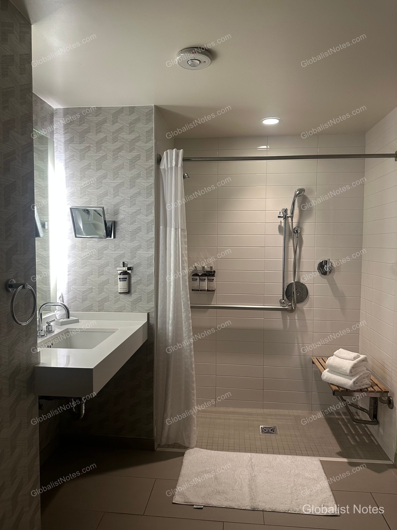 Bathroom in a One Bedroom King Suite at Hyatt Regency Los Angeles International Airport. The wheelchair-accessible shower features grab bars and a fold-down shower seat, with a clean vanity and mirror located adjacent.