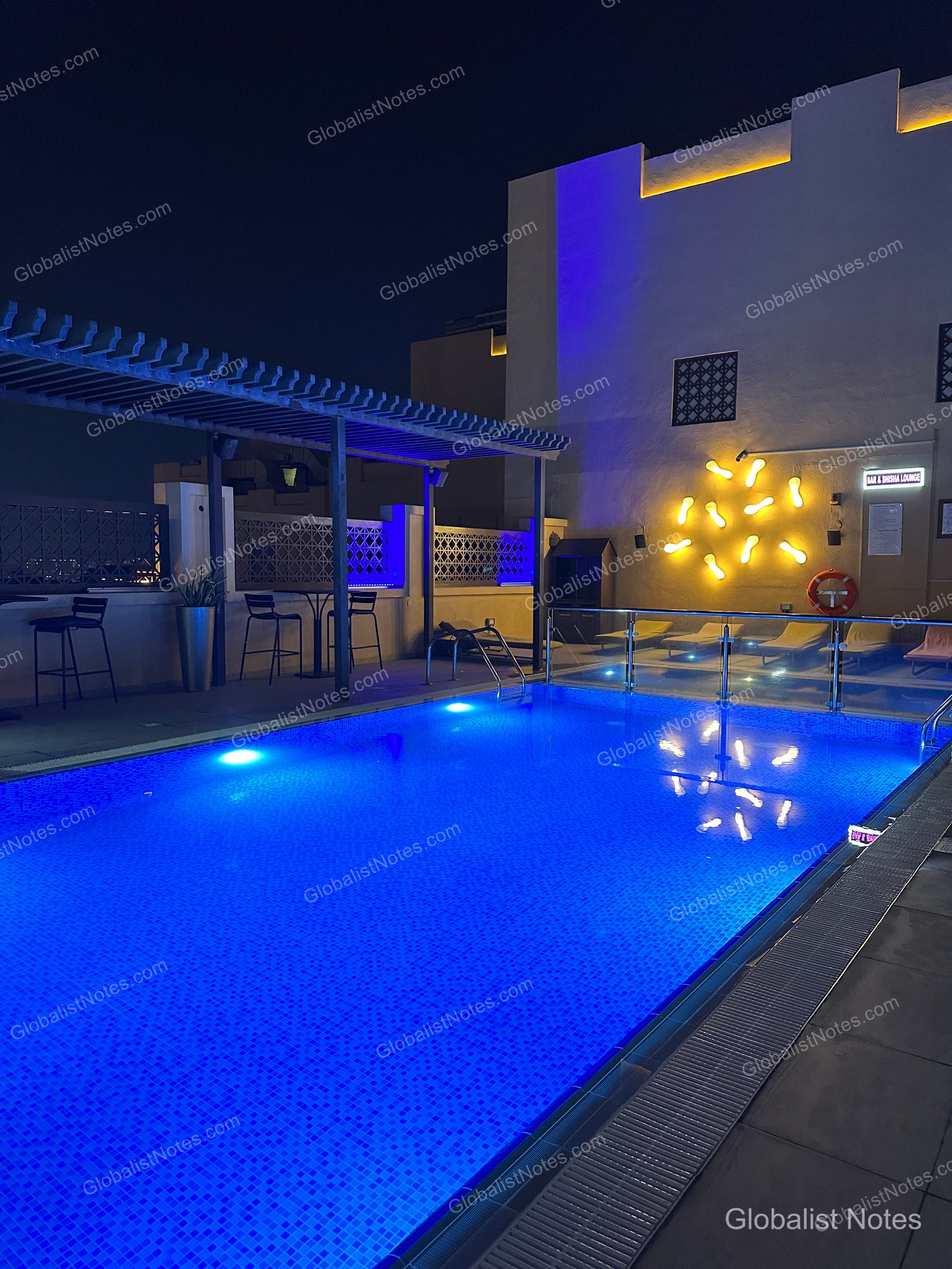 Hyatt Place Dubai Wasl District 的戶外泳池夜景。長方形泳池點亮藍色燈光，一旁設有帶涼棚的休憩區與牆面裝飾燈，泳池邊緣則裝有玻璃護欄。
