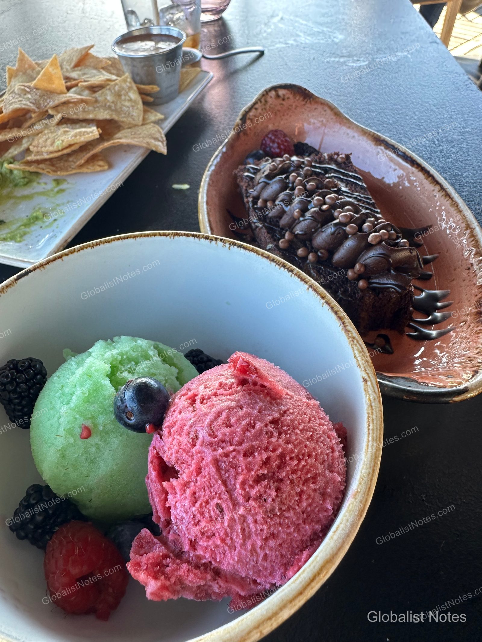 Lunch served at Alila Ventana Big Sur, featuring a chocolate cake, raspberry and lime sorbet, and a side of nachos with guacamole on a black table.