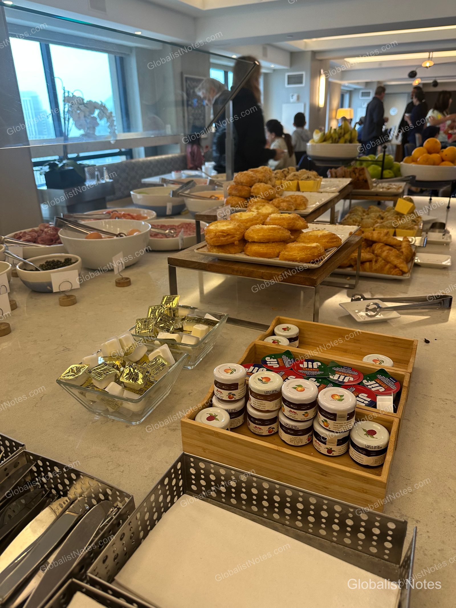 Manchester Grand Hyatt San Diego 早餐自助餐區，大理石桌面上整齊擺放著各式麵包、奶油、果醬與花生醬。後方備有水果與沙拉，背景可見用餐的住客。