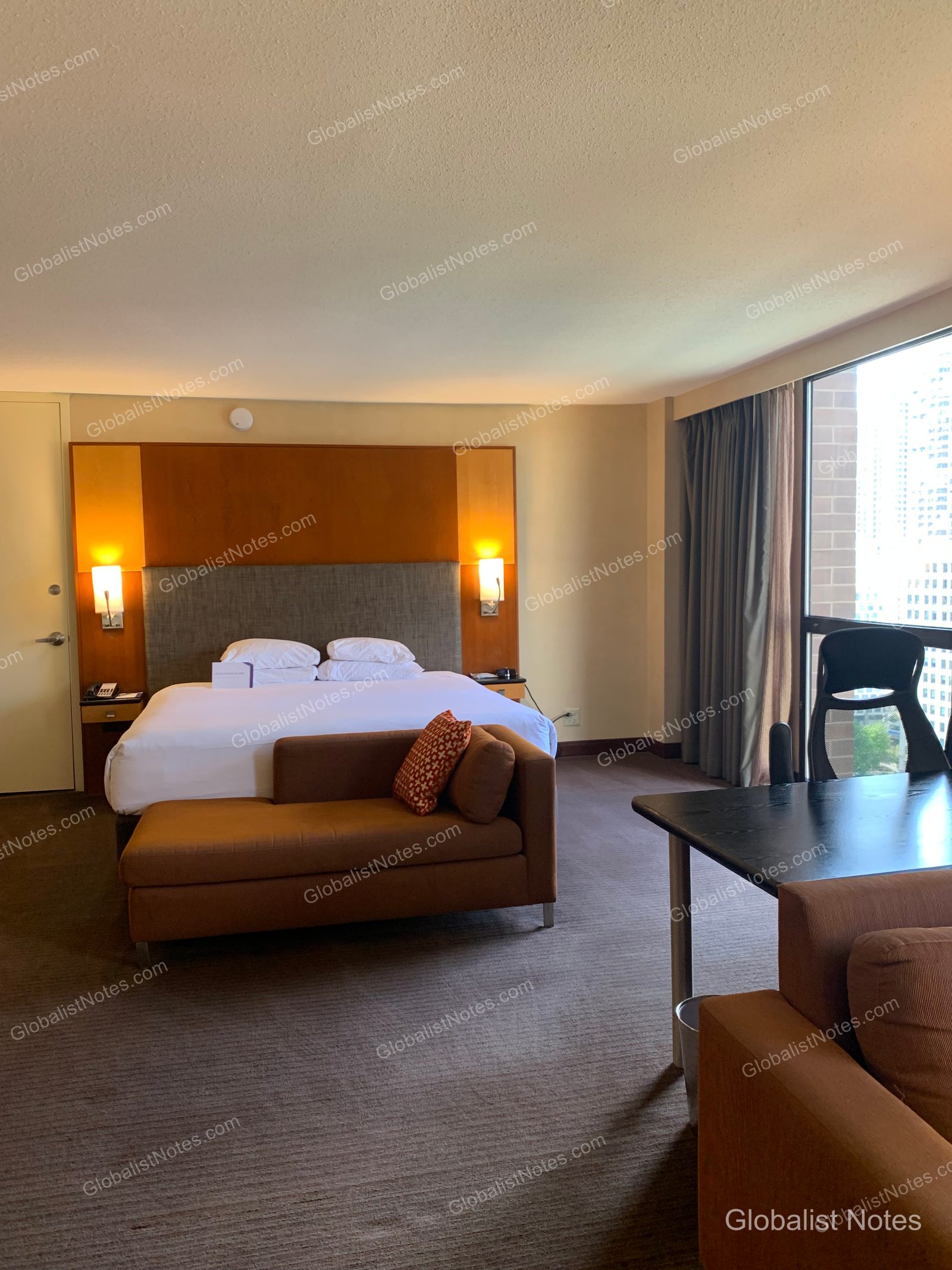 Hyatt Regency Chicagoのジュニアスイートルーム。キングベッド、デイベッド、ワークデスクが配置され、右側の大きな窓からはシカゴのビル群が見渡せます。