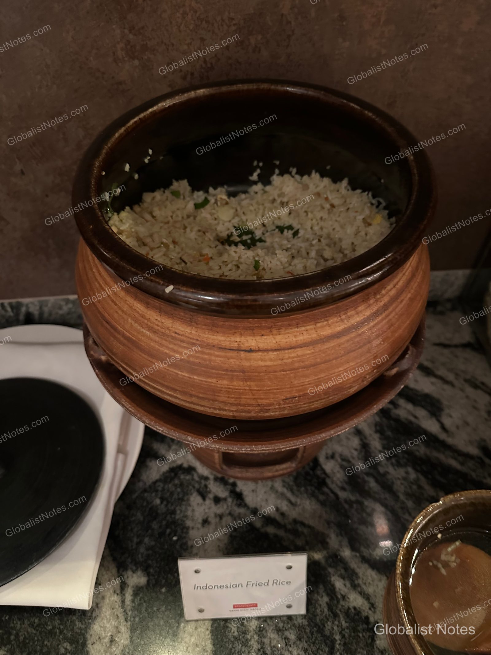 Indonesian fried rice served in a brown ceramic pot at the Grand Hyatt Jakarta lounge, with a small sign labeled 'Indonesian Fried Rice' in front.