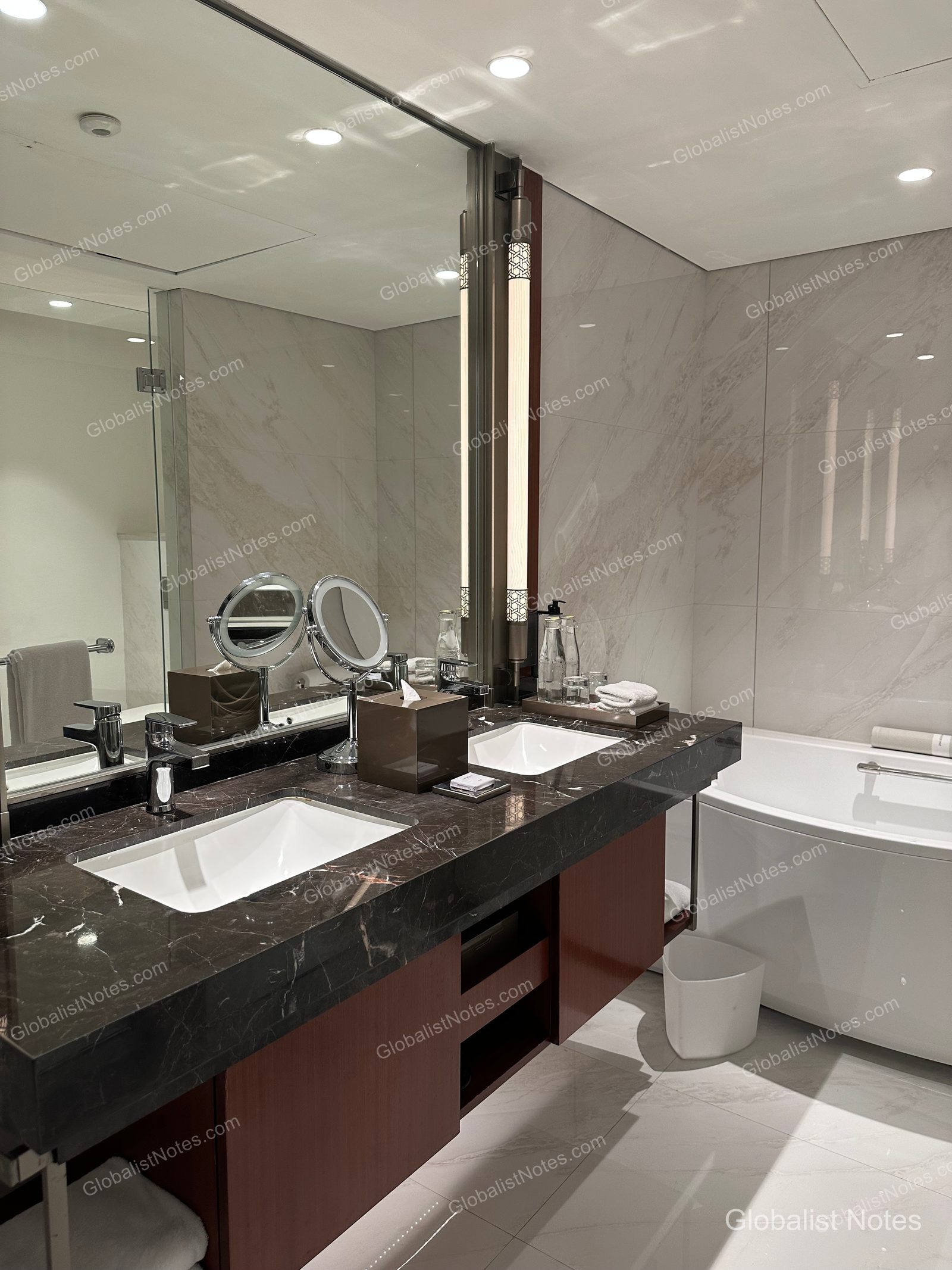 Marble vanity in the Grand Suite bathroom at Grand Hyatt Jakarta. The dark marble countertop features dual sinks and a magnifying mirror, with a white bathtub positioned to the right.