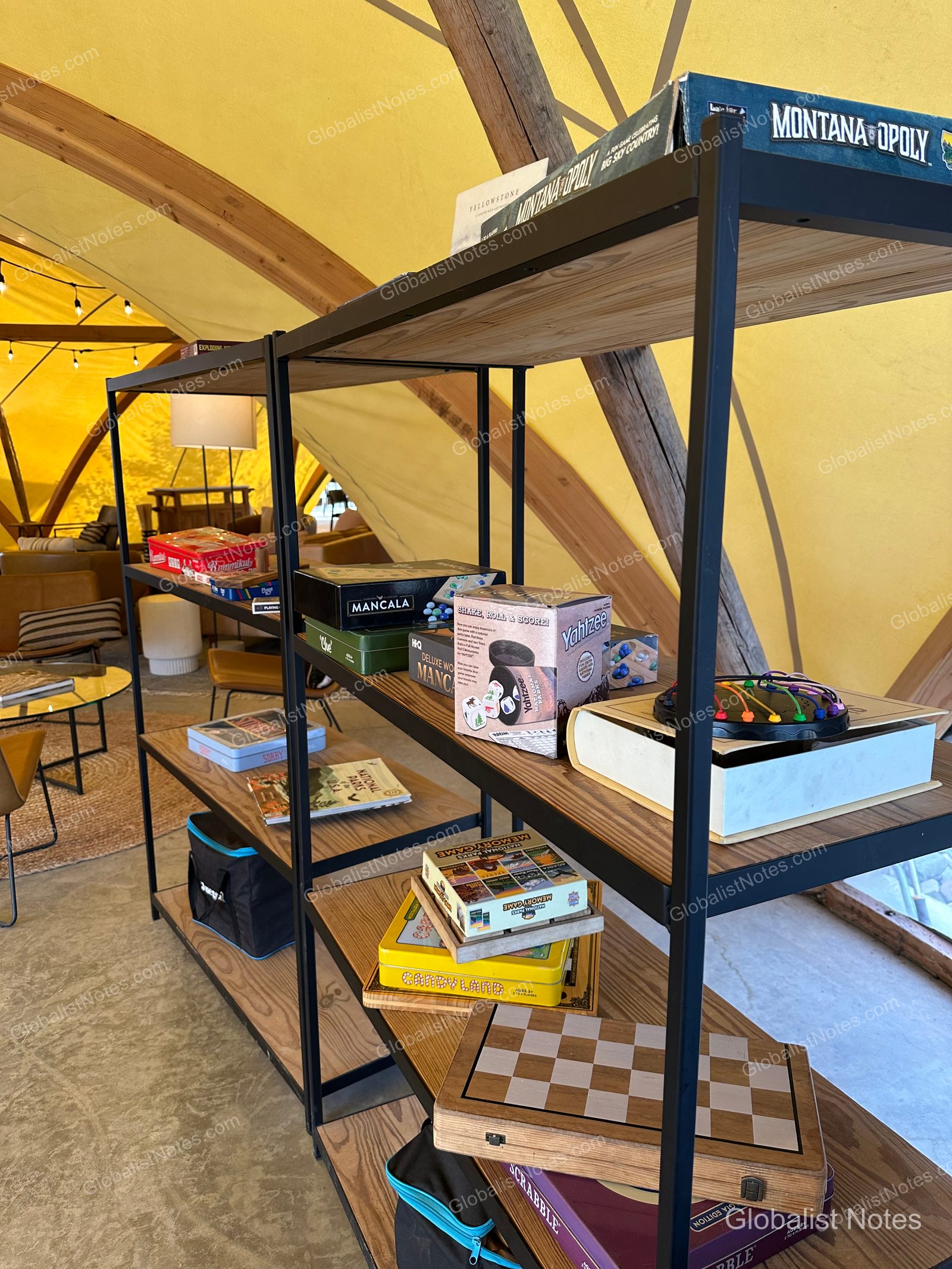 Under Canvas North Yellowstoneの共用テント内。棚にはモノポリーやヤッツィーなどのボードゲームが並び、背景にはテントの幕とラウンジ家具が見える。