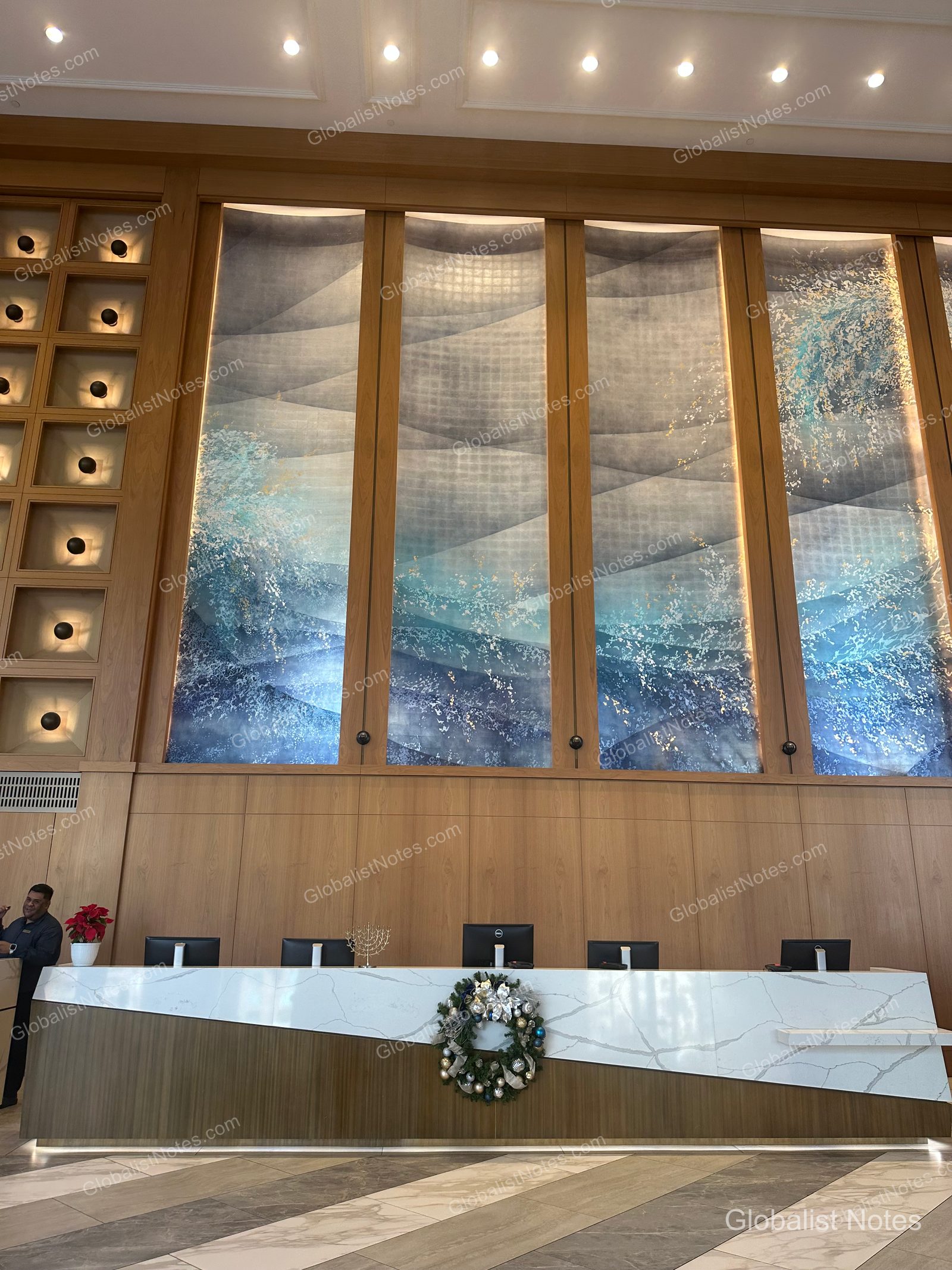 Manchester Grand Hyatt San Diego 大廳櫃檯全景。大理石檯面的長櫃檯上裝飾著聖誕花圈，後方牆面設有結合燈光效果的波浪造型大型藝術品。