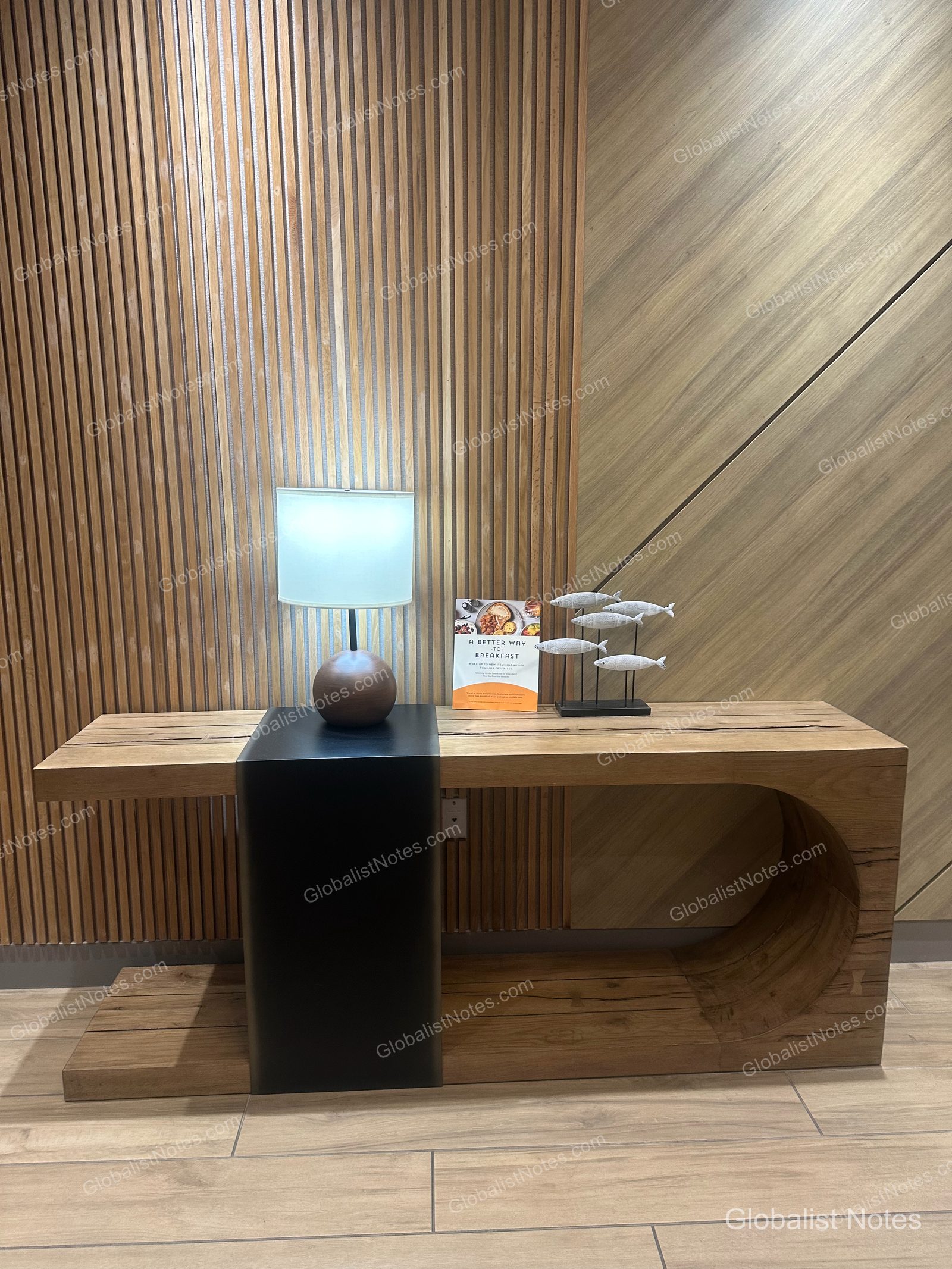 Hyatt Place Flagstaffのロビー。ウッドパネルの壁を背景に、照明や朝食案内、魚のオブジェが置かれたモダンな木製コンソールテーブルが配されています。