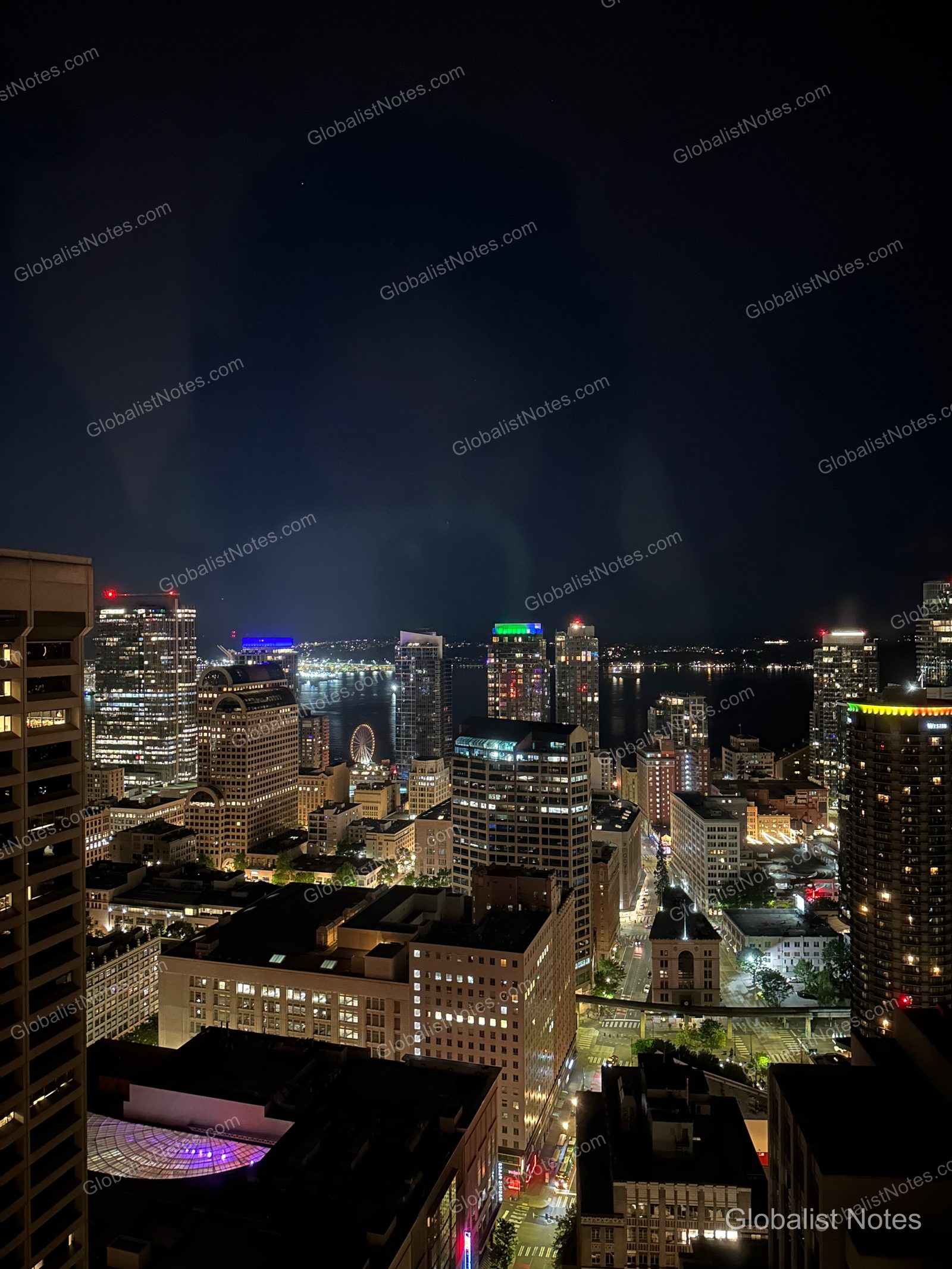 Night view of the Seattle cityscape from a Hyatt Regency Seattle guest room window, featuring illuminated high-rise buildings and the waterfront ferris wheel in the distance.