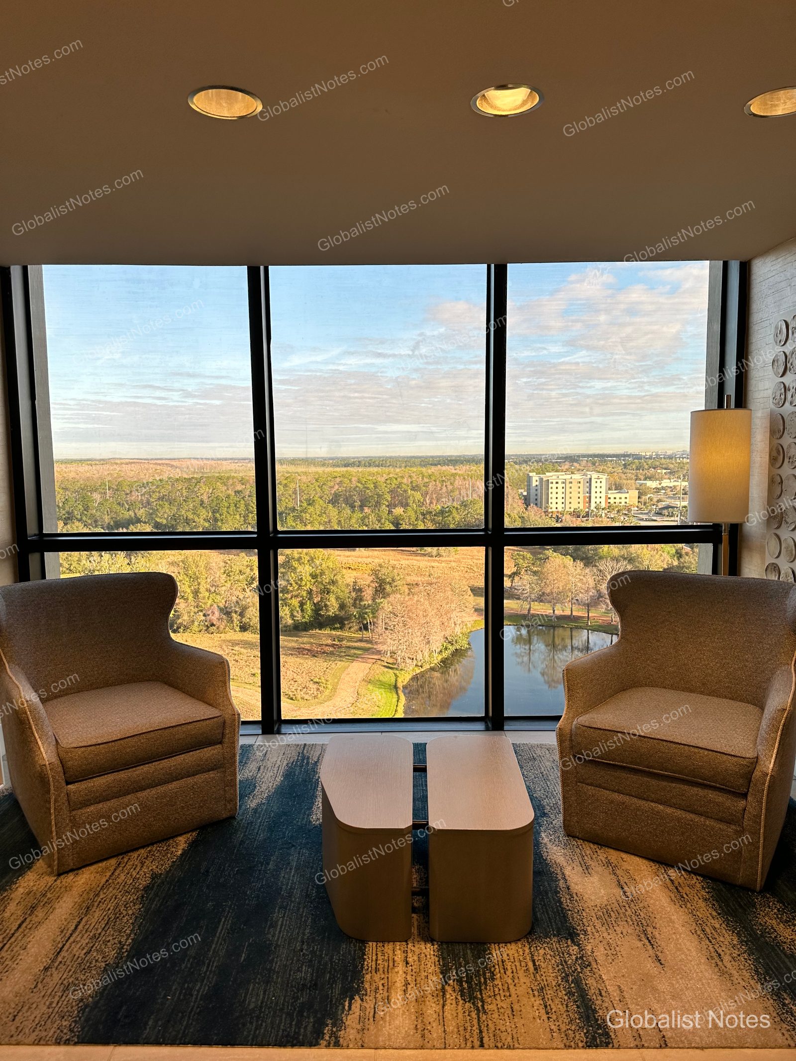 Two armchairs and a small table placed by the window in a guest room at Hyatt Regency Grand Cypress. The floor-to-ceiling windows overlook a view of the lake and surrounding forest, and the room features patterned carpeting.