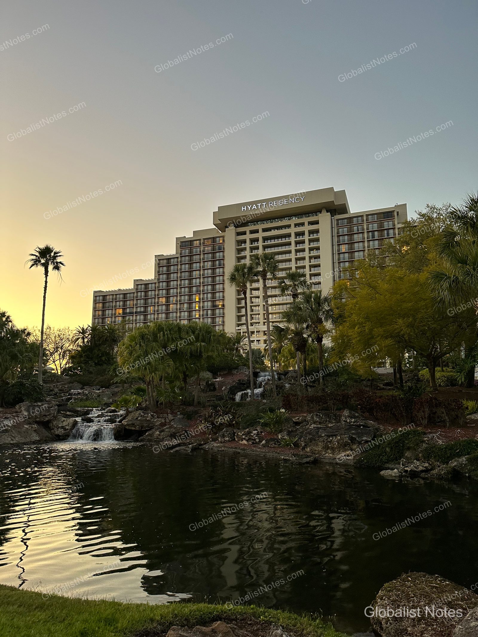Exterior view of Hyatt Regency Grand Cypress in Orlando at sunset, featuring the terraced building architecture, a pond, and an artificial waterfall.