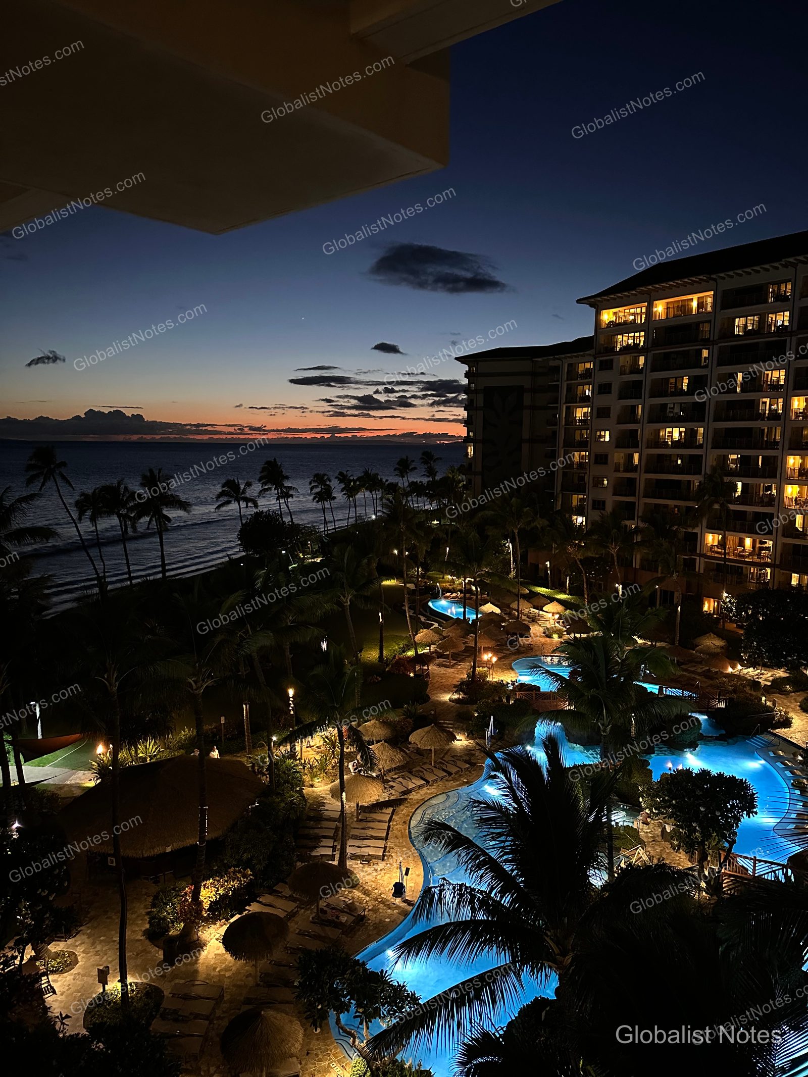 Night view from Hyatt Regency Maui Resort and Spa in Lahaina, Hawaii. The scene shows the illuminated pool and palm trees under a dark sky, with the ocean horizon in the distance and warm lights glowing from the guest room windows.