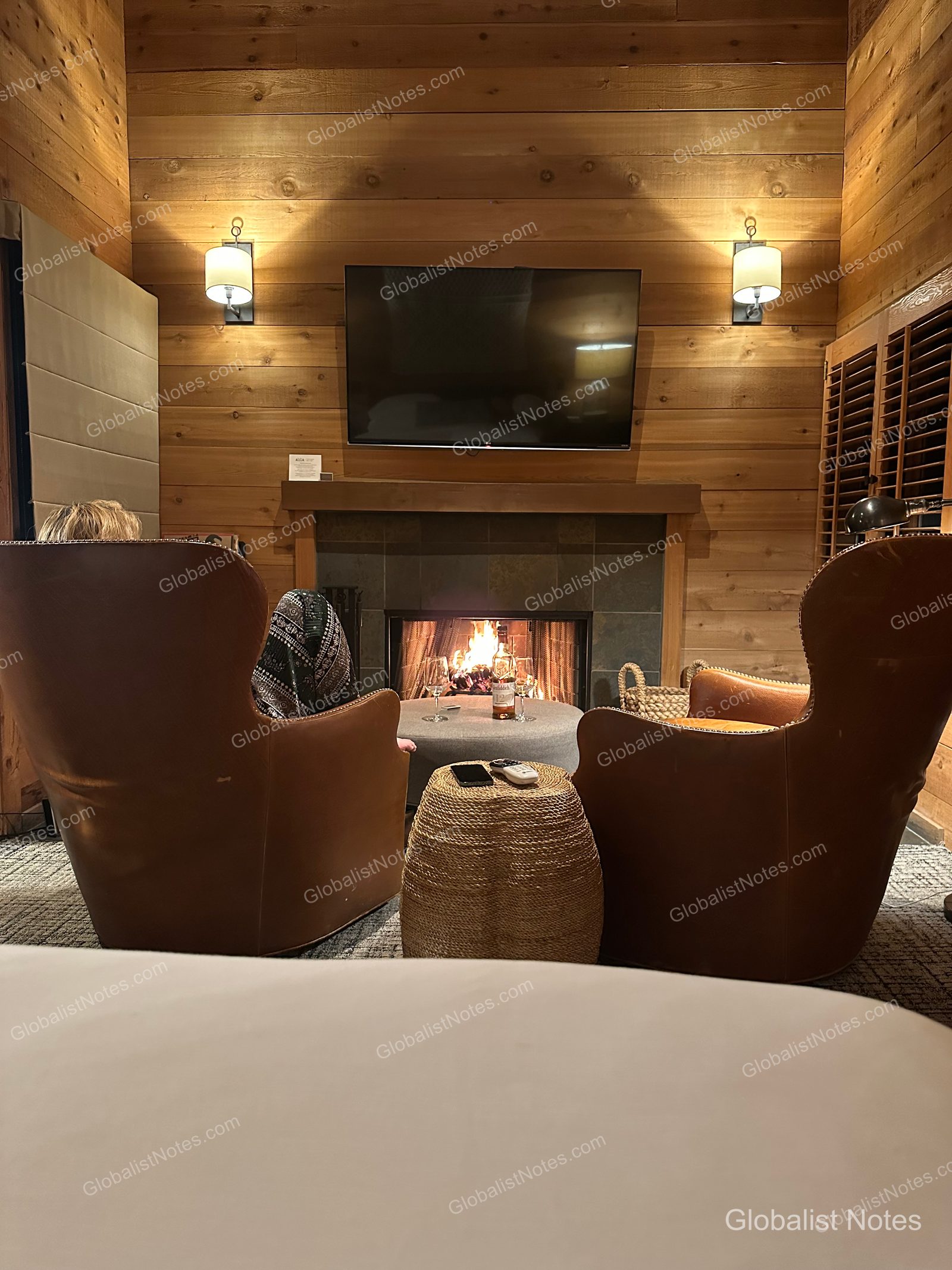A cozy room interior at Alila Ventana Big Sur featuring two leather armchairs and a small table in front of a fireplace, with a TV mounted on the wall.