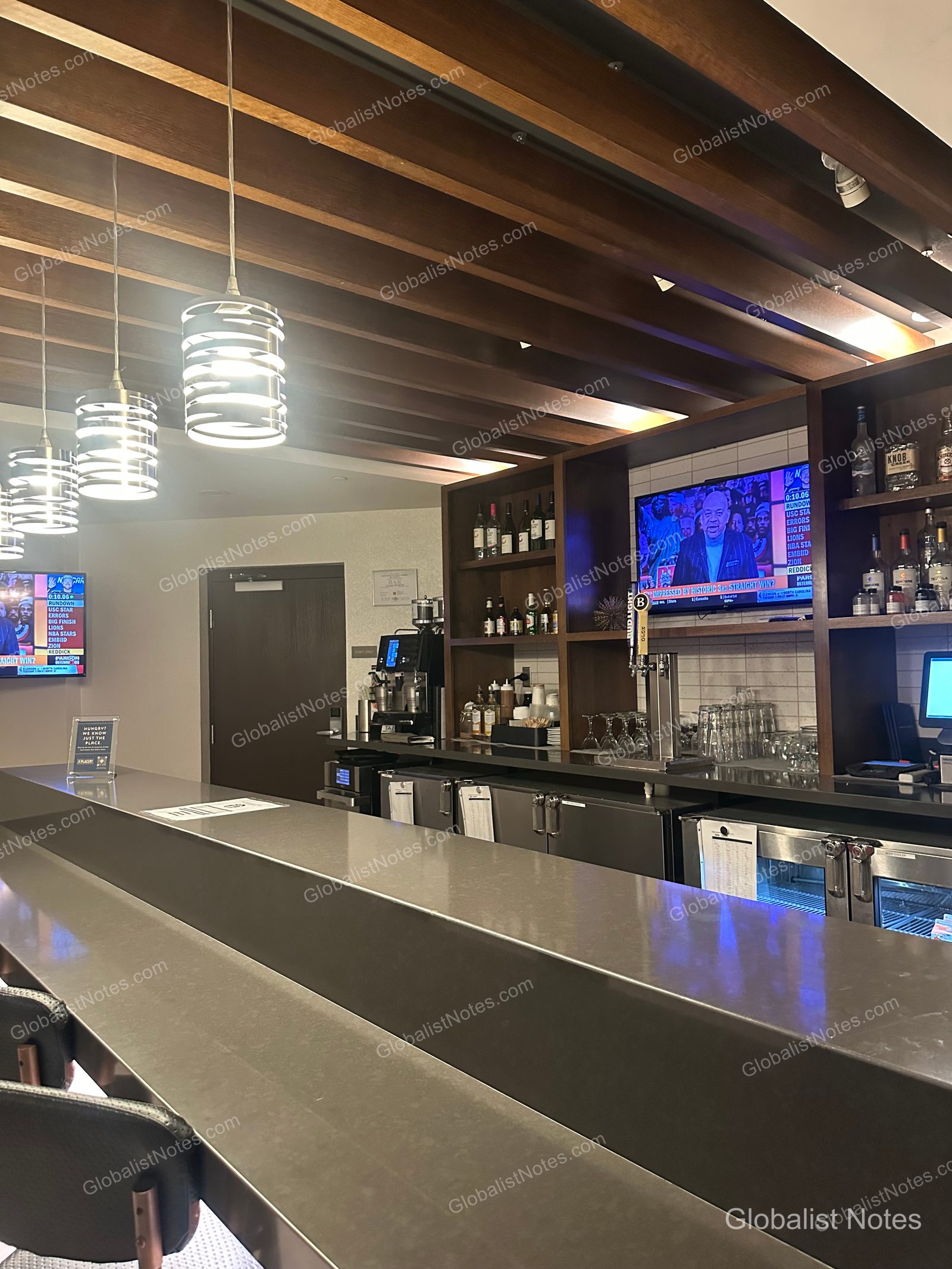 Hyatt Place Tucson-Central 酒吧區，設有灰色長吧台與黑色高腳椅。天花板裝飾木板與吊燈，牆面層架陳列酒類，並設有電視螢幕。