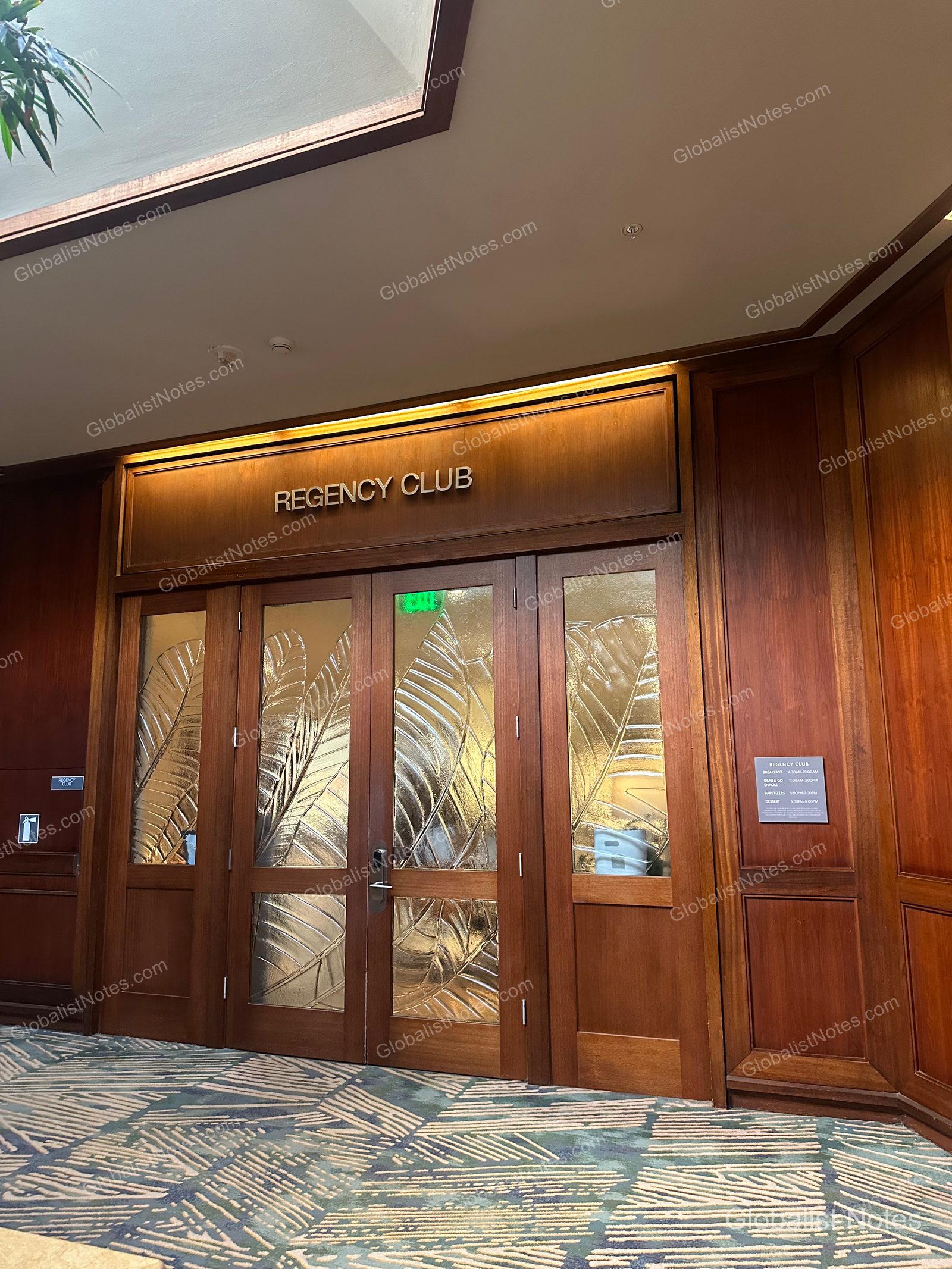 Entrance to the Regency Club at Hyatt Regency Maui Resort and Spa. The wooden door features glass panels with a leaf pattern and a 'REGENCY CLUB' sign above it, with a sign detailing operating hours mounted on the wall to the right.