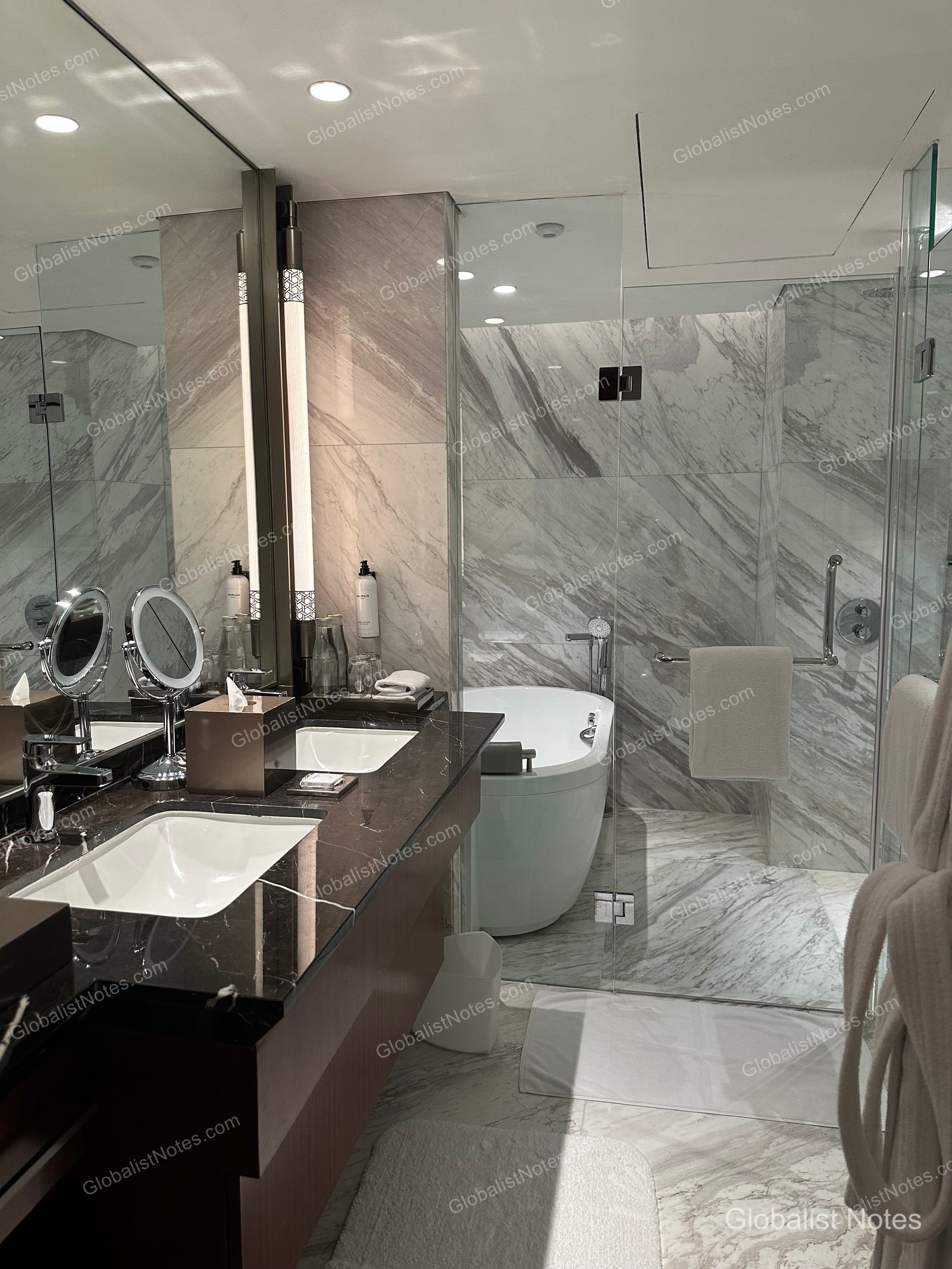 Bathroom of a Grand Suite at Grand Hyatt Jakarta. The space features marble walls and flooring, a double vanity, and a separate soaking tub and shower area behind a glass partition.