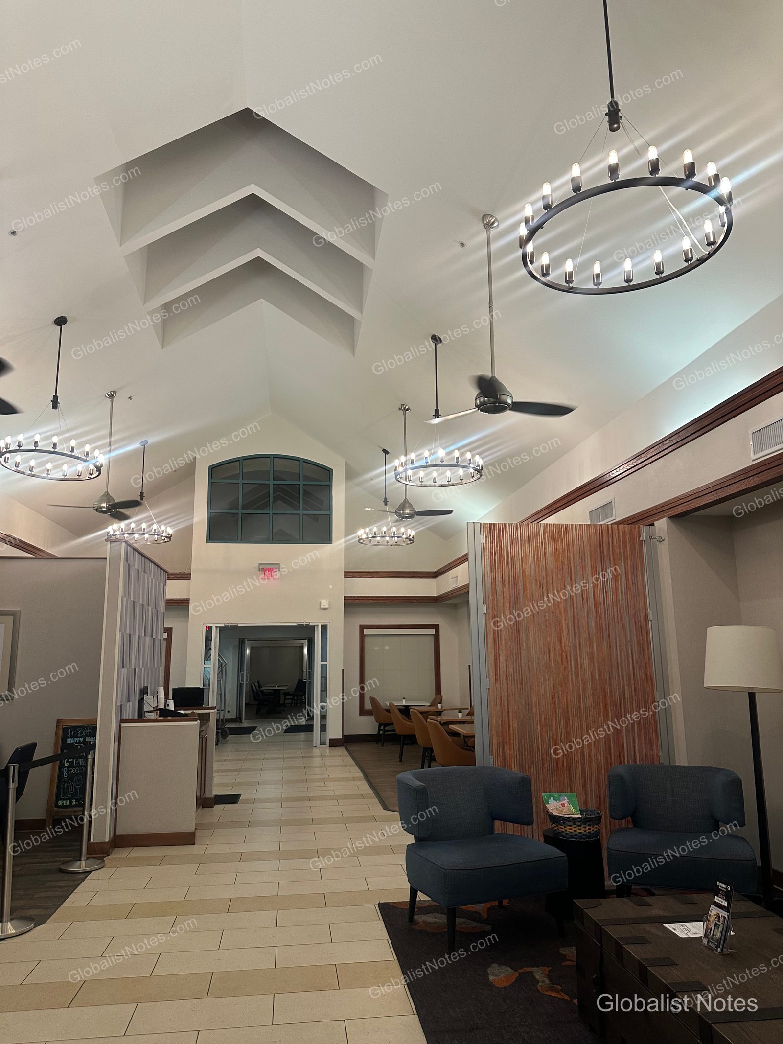 Hyatt House Scottsdale/Old Townのロビー。切妻天井とシャンデリアが印象的な広々とした空間で、正面にフロントデスク、右手に青いアームチェアを配した休憩スペースがあります。