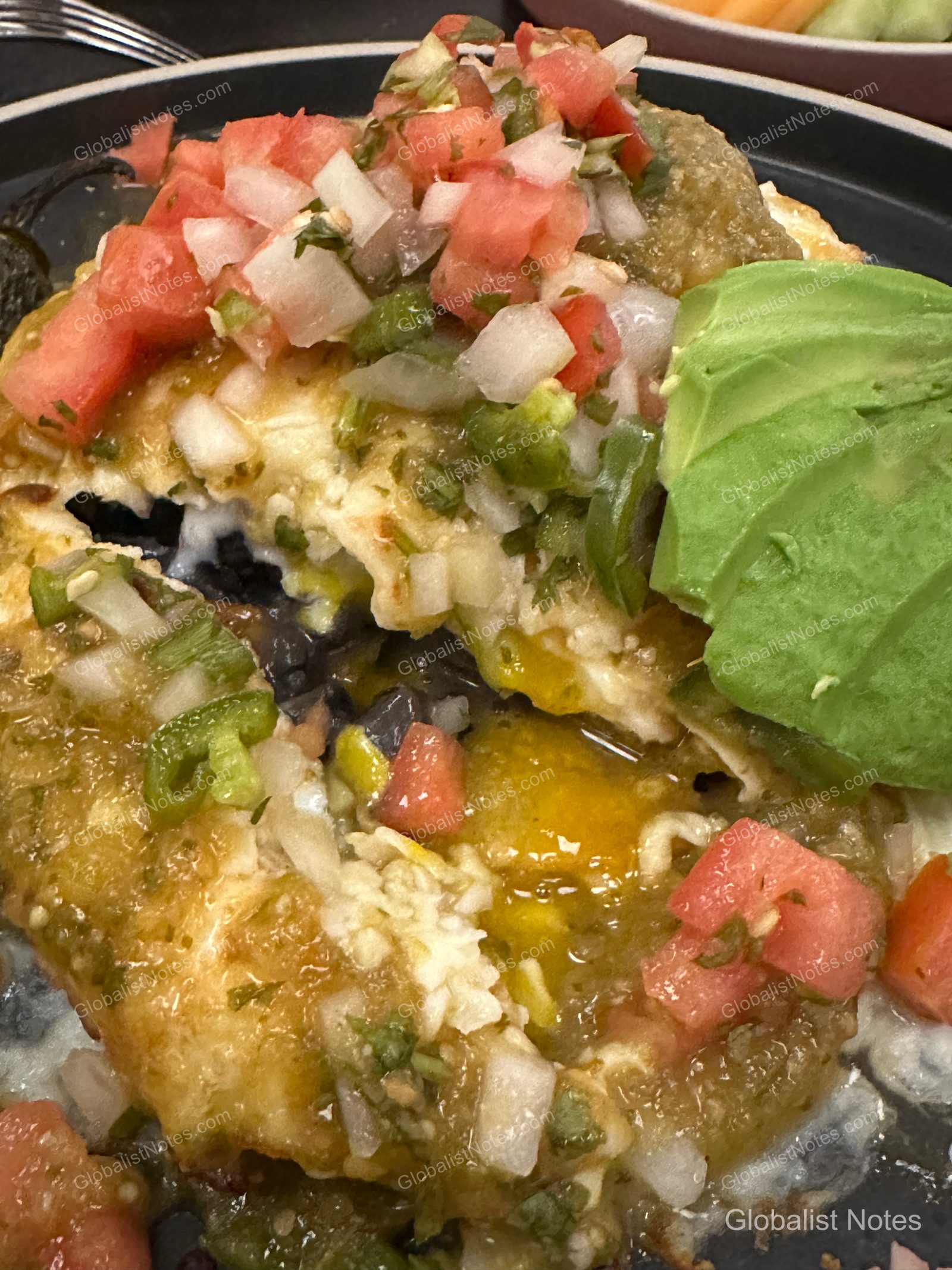 Mexican-style egg dish served for breakfast at Hyatt Regency Los Angeles International Airport. The eggs are topped with green salsa, fresh tomato, onion, and jalapeño salsa, and sliced avocado, served over a bed of black beans.