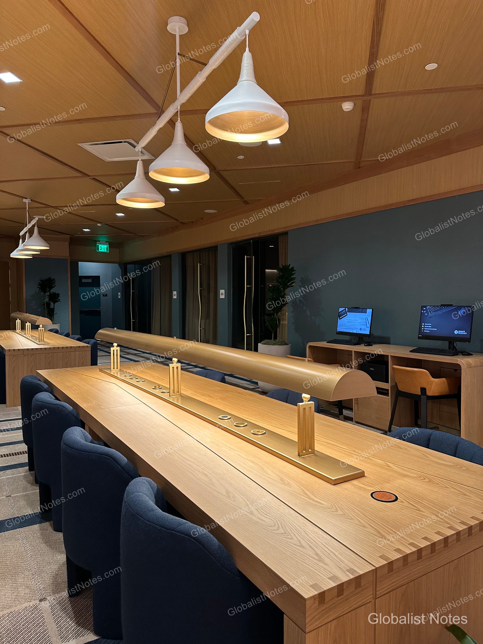 Hyatt Regency Irvine 商務中心內部，設有長型原木桌與海軍藍座椅，天花板懸掛白色吊燈。牆邊設有配備電腦的工作站，環境安靜整潔。