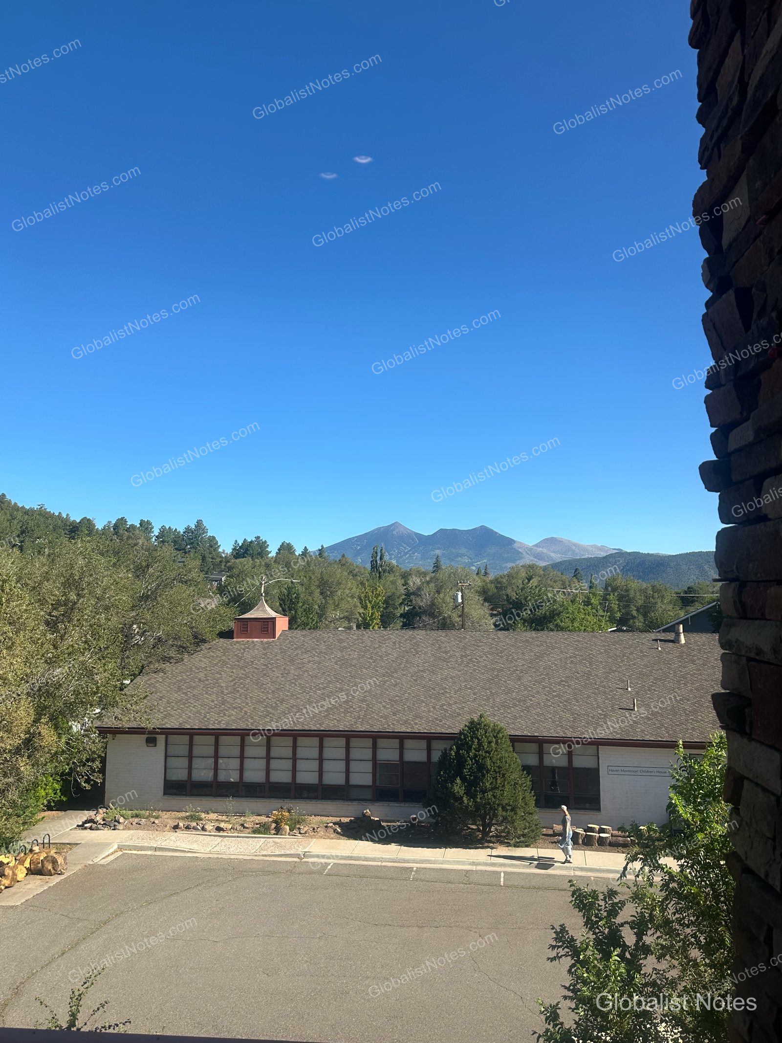 Hyatt Place Flagstaffの客室の窓から望む、晴れた空と青い山脈、眼下の建物と駐車場の風景。