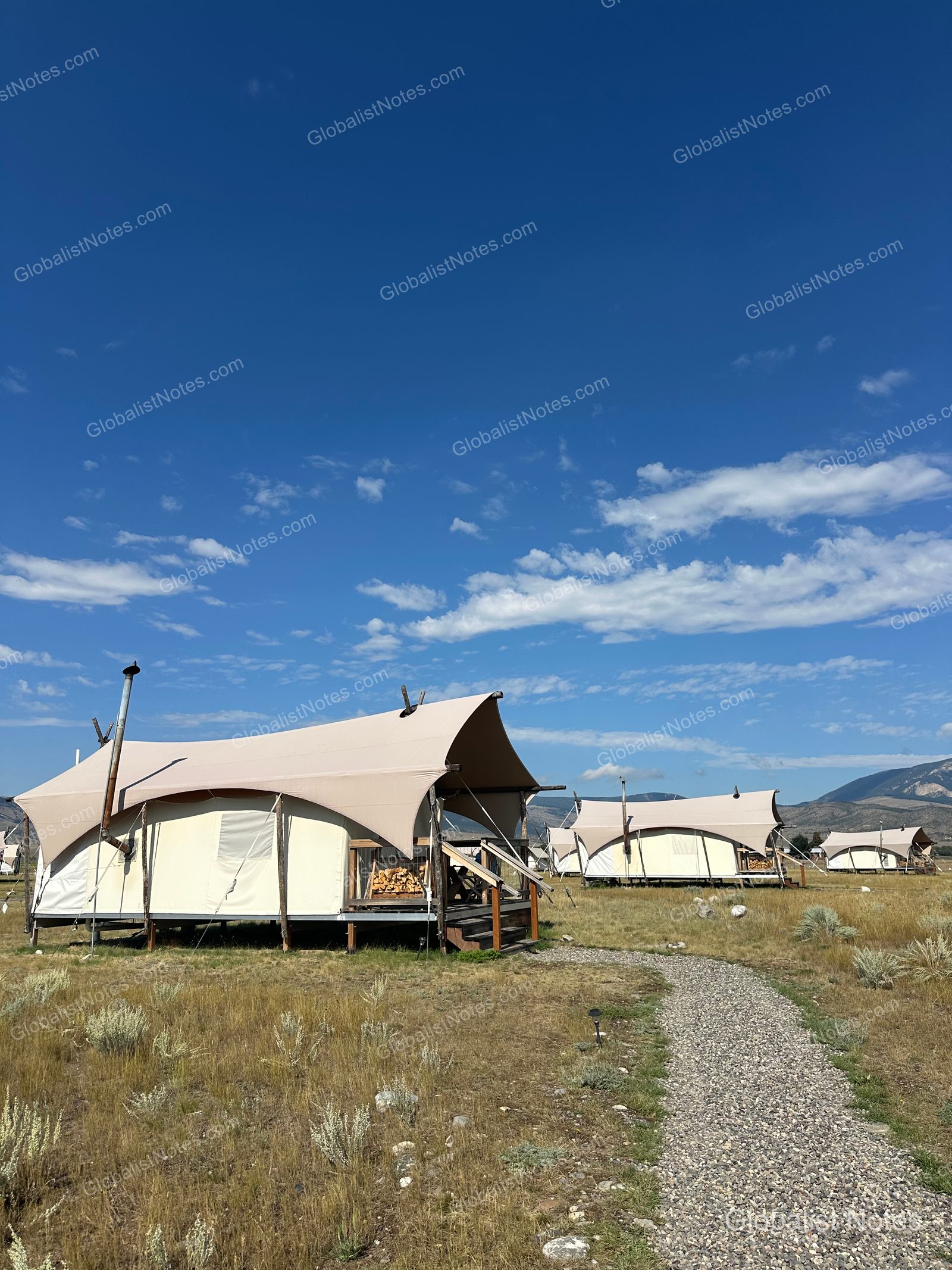 パラダイスバレーに位置するUnder Canvas North Yellowstoneのテント群。草原にテントが並び、各テントの前にはウッドデッキと薪が置かれています。