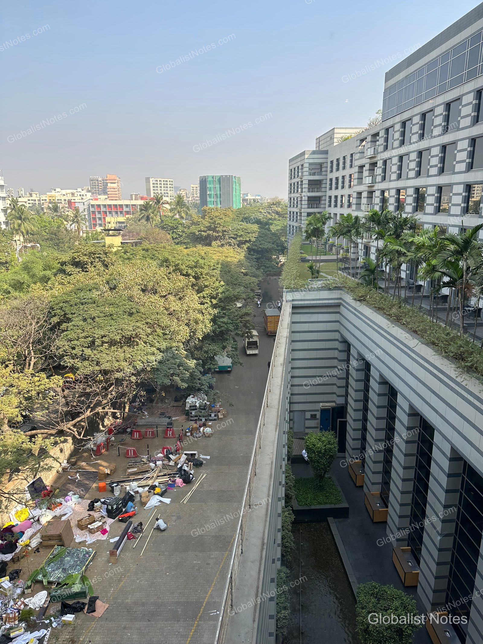 A view from the Veranda Suite King at Grand Hyatt Mumbai Hotel & Residences, showing the hotel's modern exterior and landscaping alongside a wooded, undeveloped lot littered with construction materials.