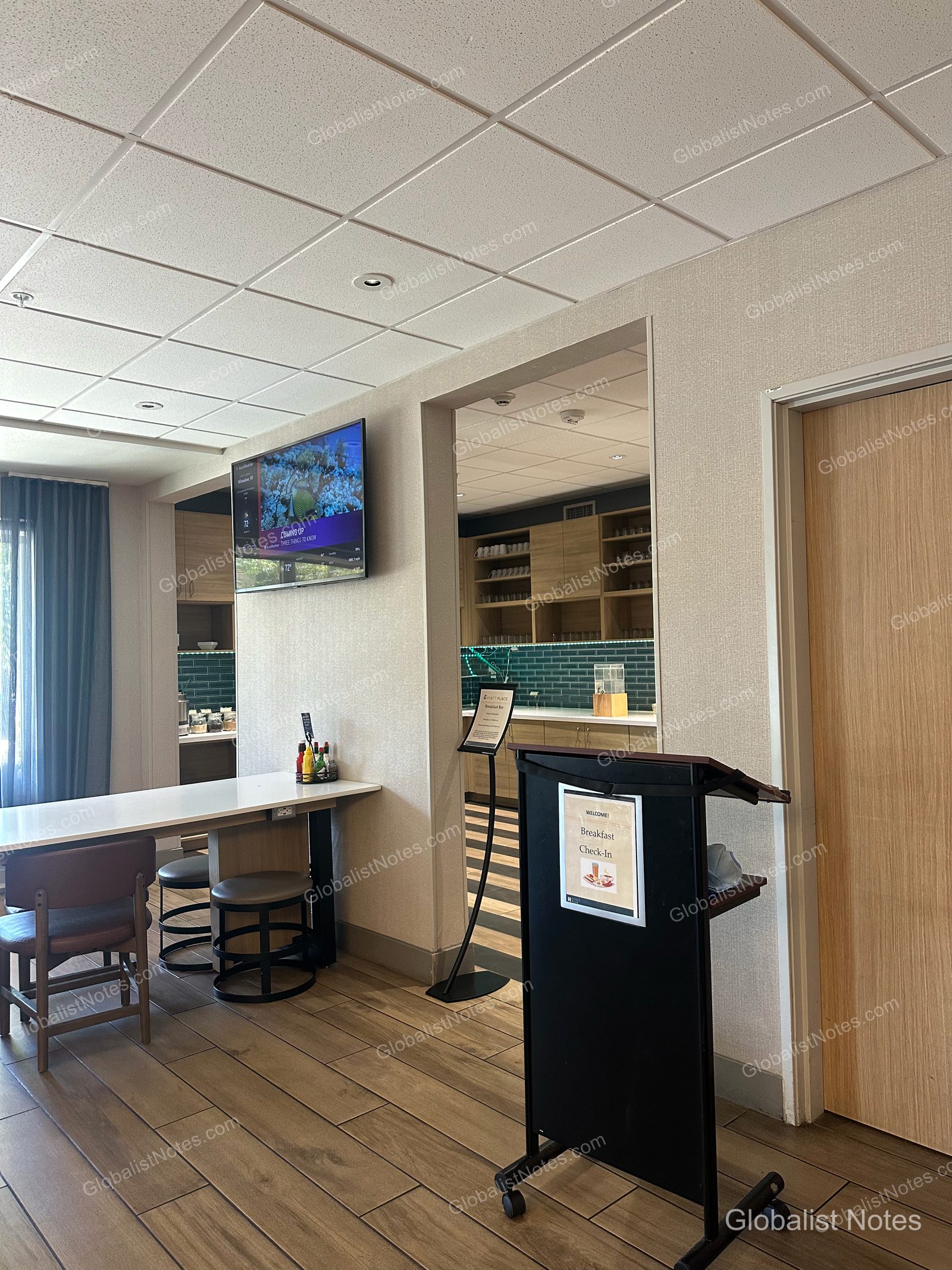 Hyatt Place Flagstaffの朝食エリア入り口。「Breakfast Check-In」と記された黒い案内板の奥に、朝食バーやテーブル席、壁掛けテレビが見えます。