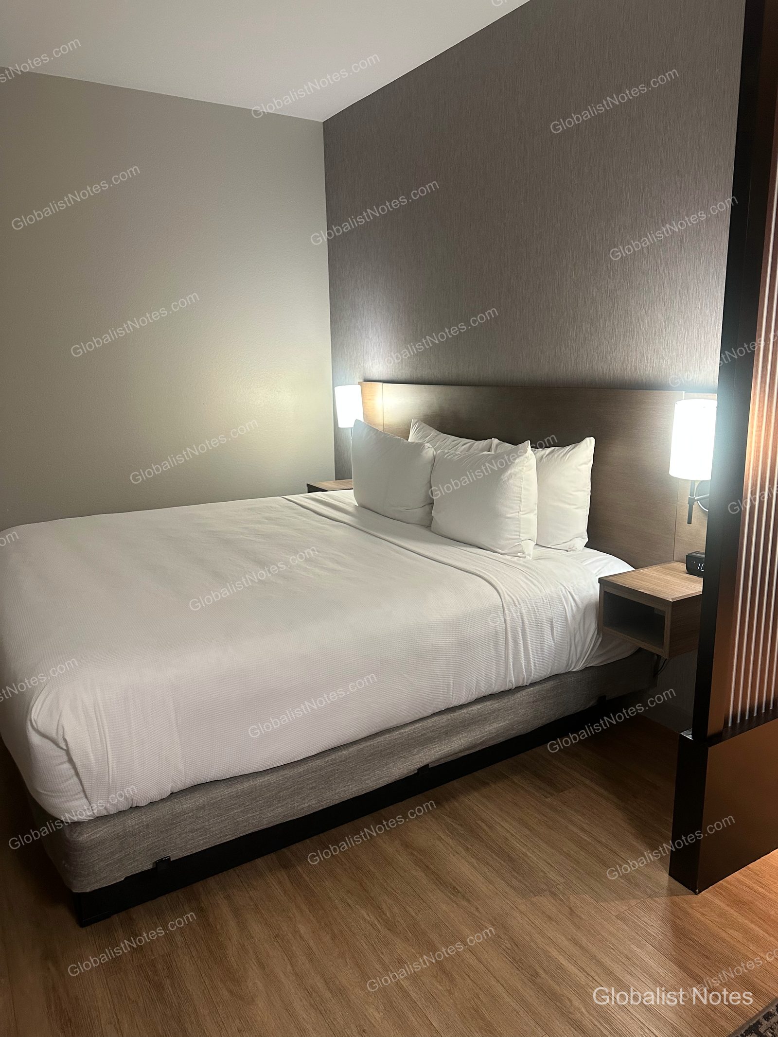 Hyatt Place Flagstaffのデラックスルーム。整えられたクイーンサイズのベッドと両サイドの照明、ウッド調の床が配されている。