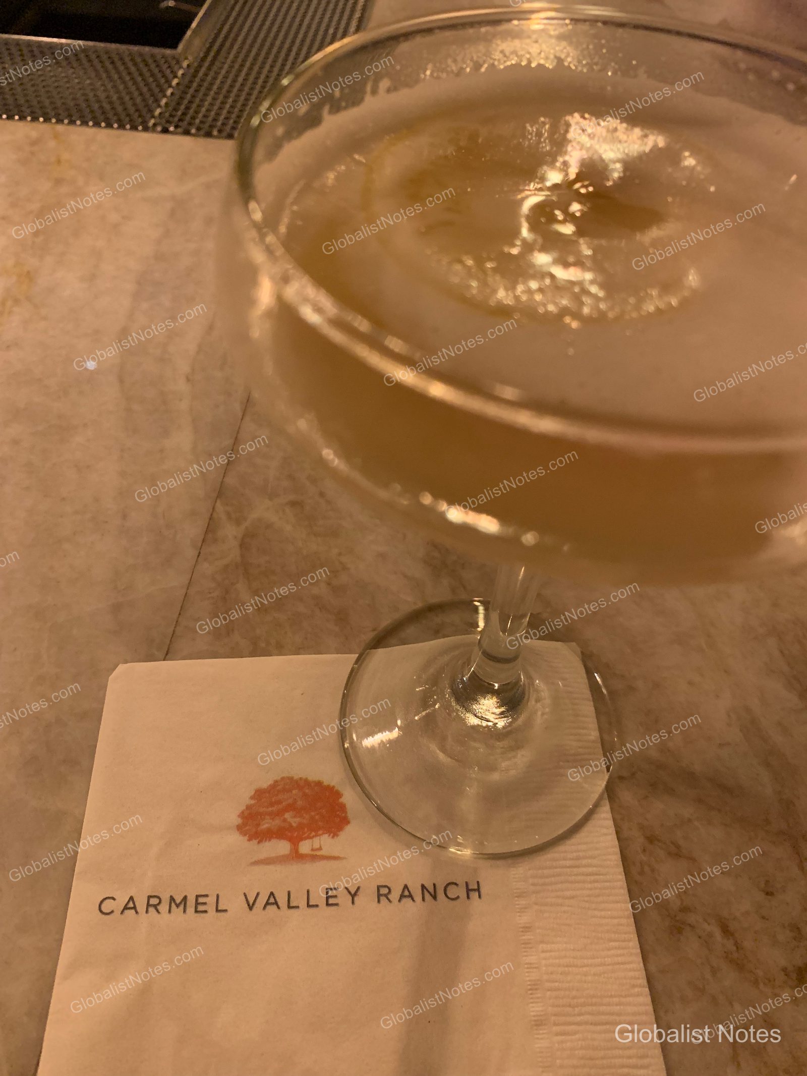 大理石のテーブルに置かれたカクテルグラス。Carmel Valley Ranchのロゴ入りナプキンが添えられ、柔らかな照明に照らされています。