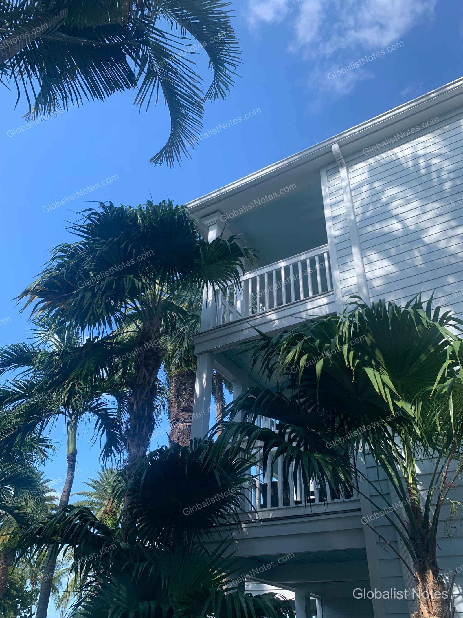 Hyatt Vacation Club at Sunset Harborの外観。白い木製サイディングの壁とバルコニーが、青空とヤシの木に囲まれています。