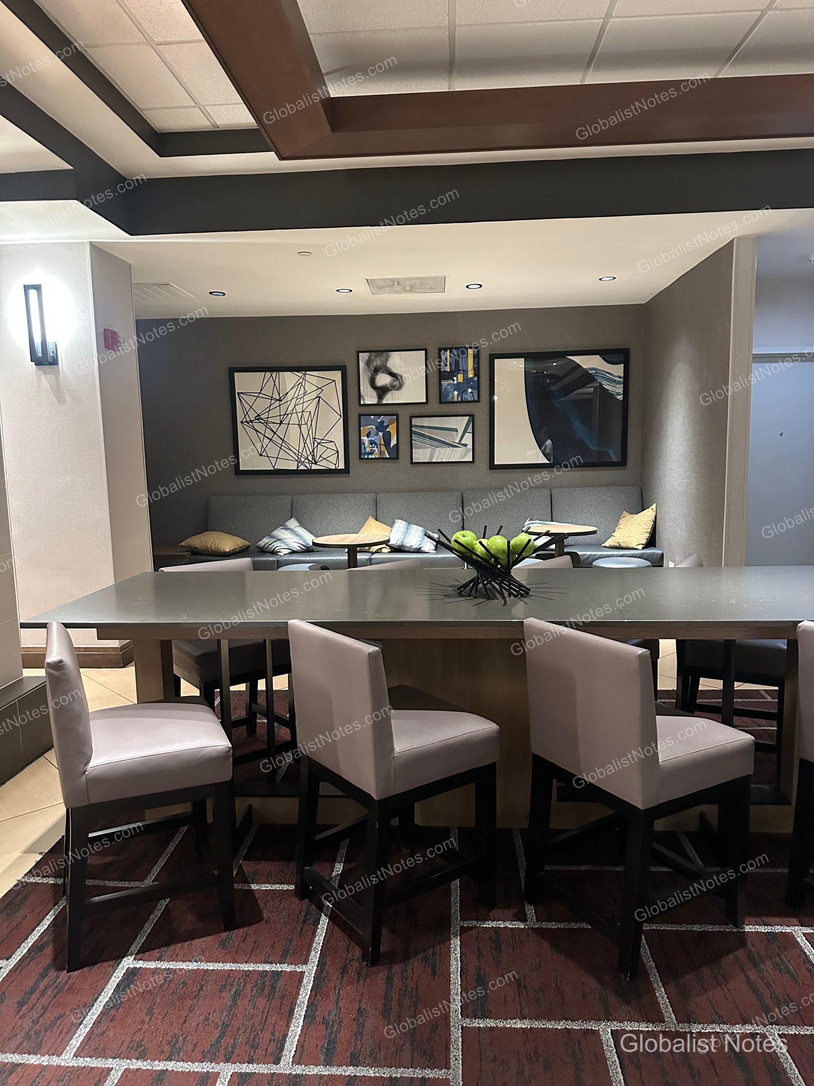 Hyatt Place El Paso Airport 的公共空間，設有長桌、灰色座椅、牆面嵌入式沙發與抽象畫。桌上擺放著青蘋果裝飾，地面鋪設幾何圖案地毯。