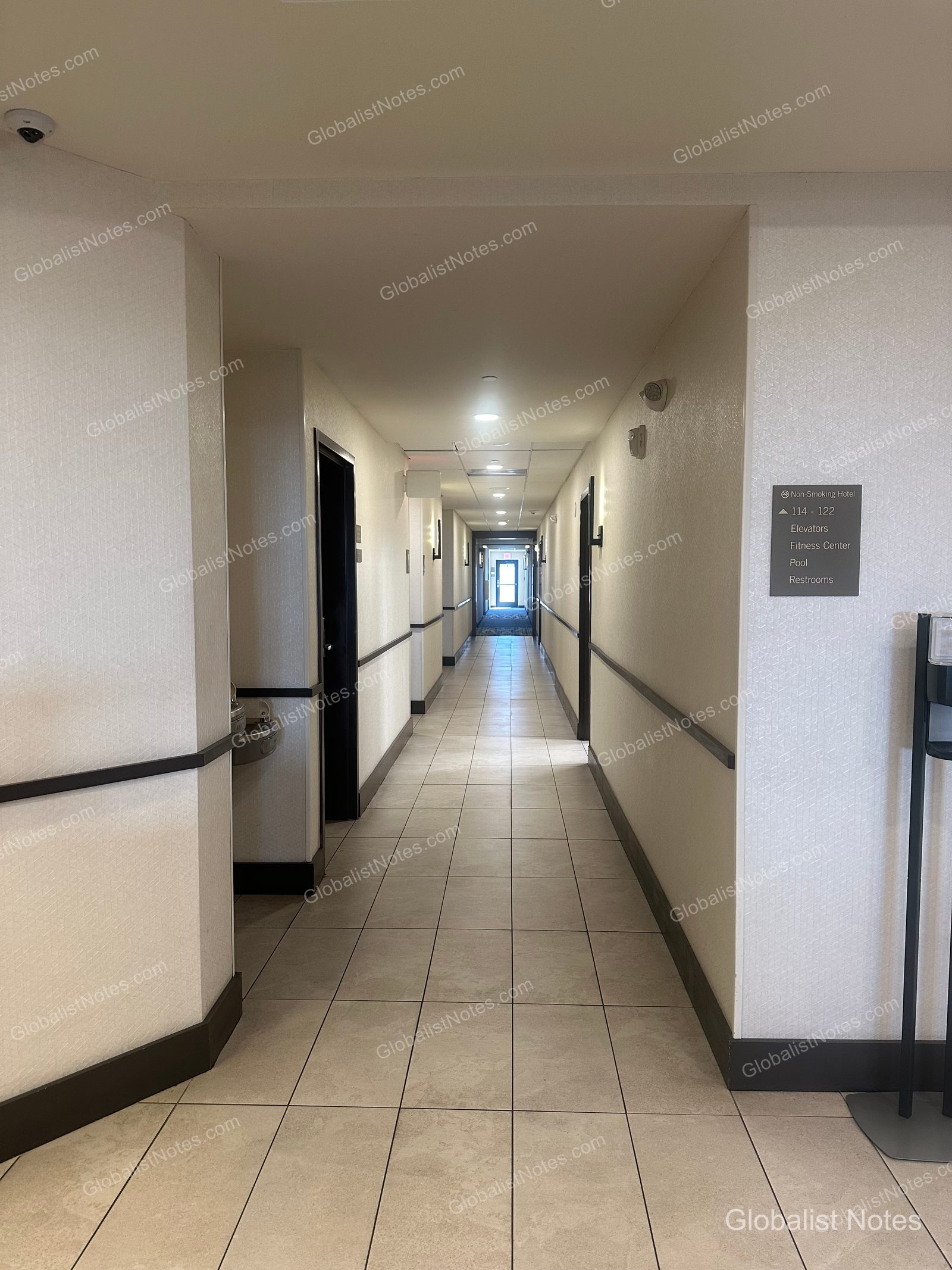 Hyatt Place Tucson-Central 明亮的走廊，鋪設米色地磚。右側牆面設有指示牌，標示電梯、健身中心與游泳池方向。