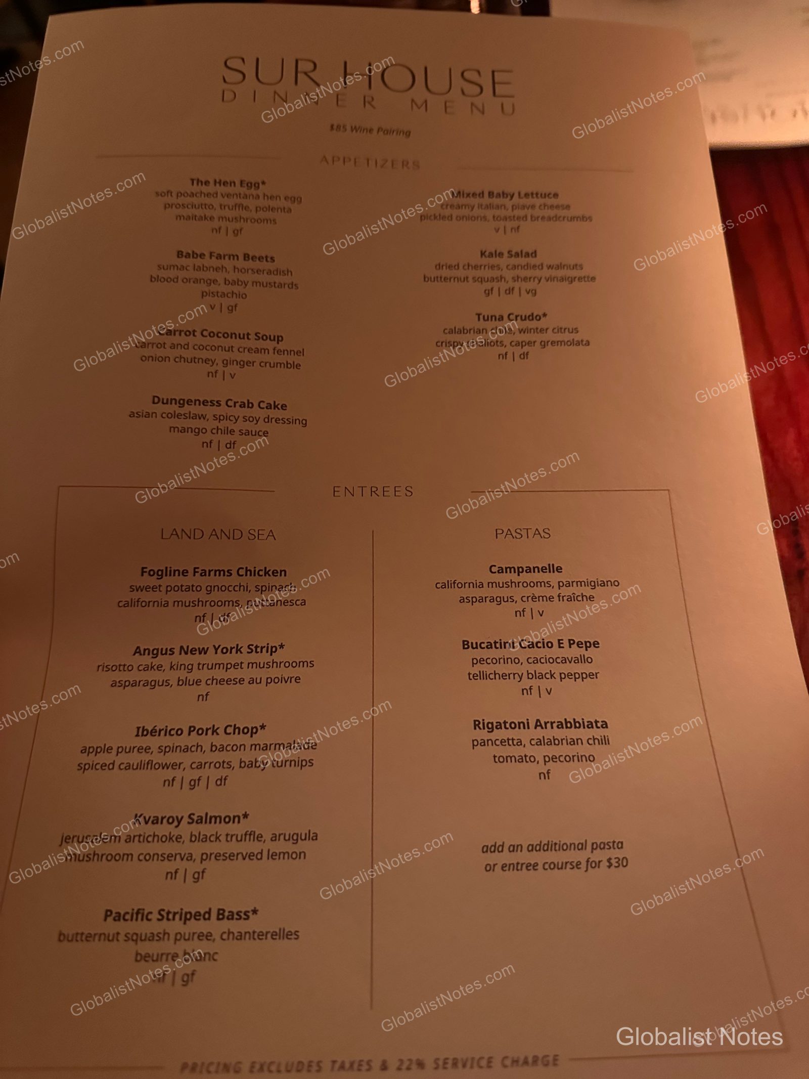 The dinner menu at The Sur House at Alila Ventana Big Sur resting on a dimly lit table. The menu lists appetizers at the top and main courses categorized by Land & Sea and Pasta at the bottom, with key ingredients and allergy information detailed for each dish.