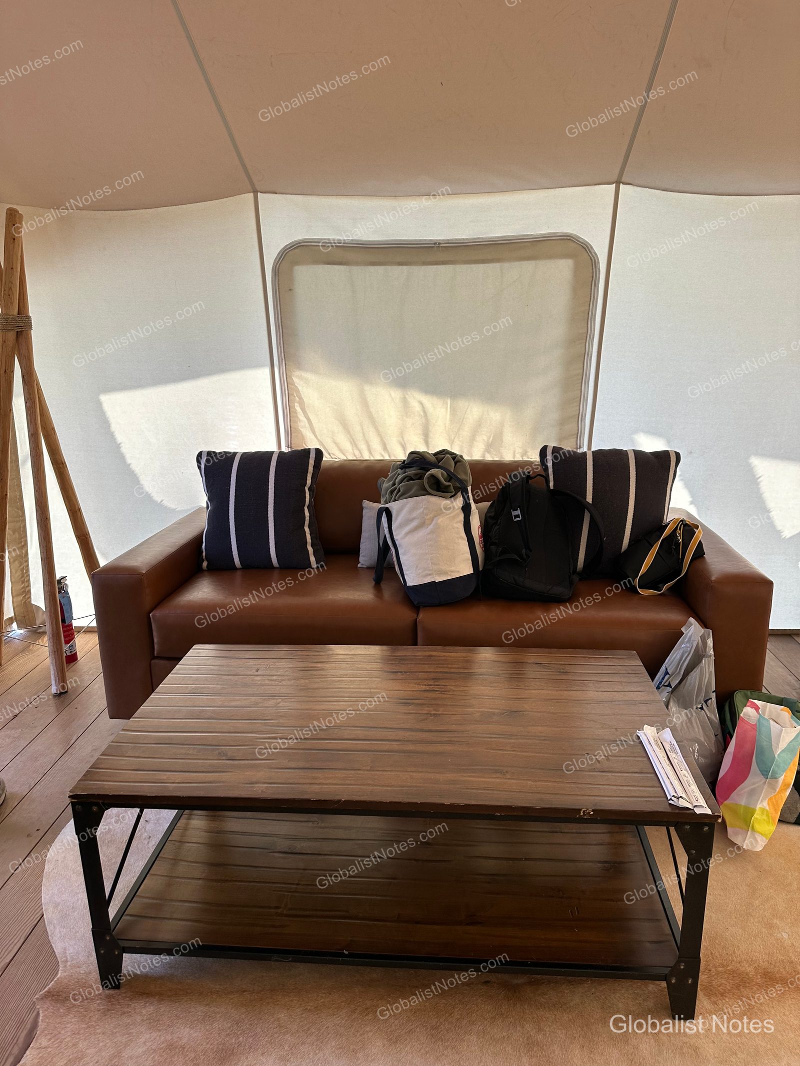 Under Canvas North Yellowstoneのテント内部。レザーソファと木製のコーヒーテーブルが置かれ、ソファにはストライプ柄のクッションが並んでいます。奥にはキャンバス地の壁と窓が見えます。
