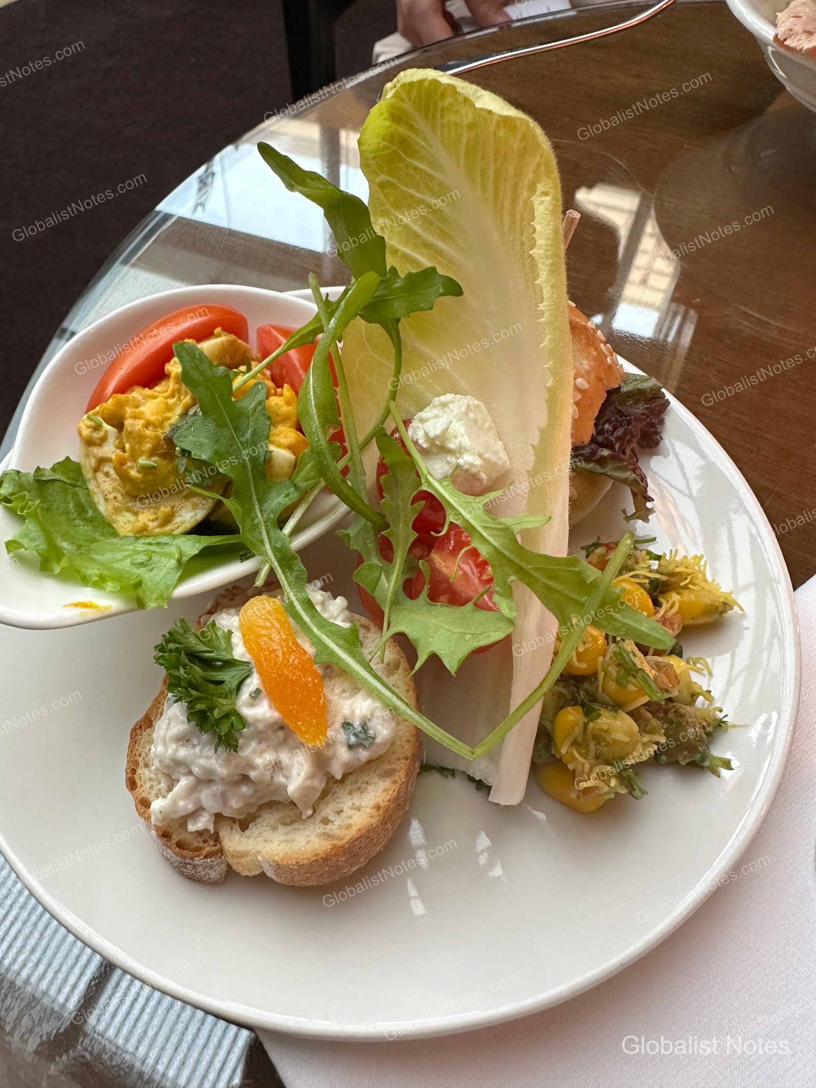 A plate from the Grand Hyatt Mumbai lounge featuring egg salad, tuna salad on baguette slices, and a side of fresh vegetables and corn salad.