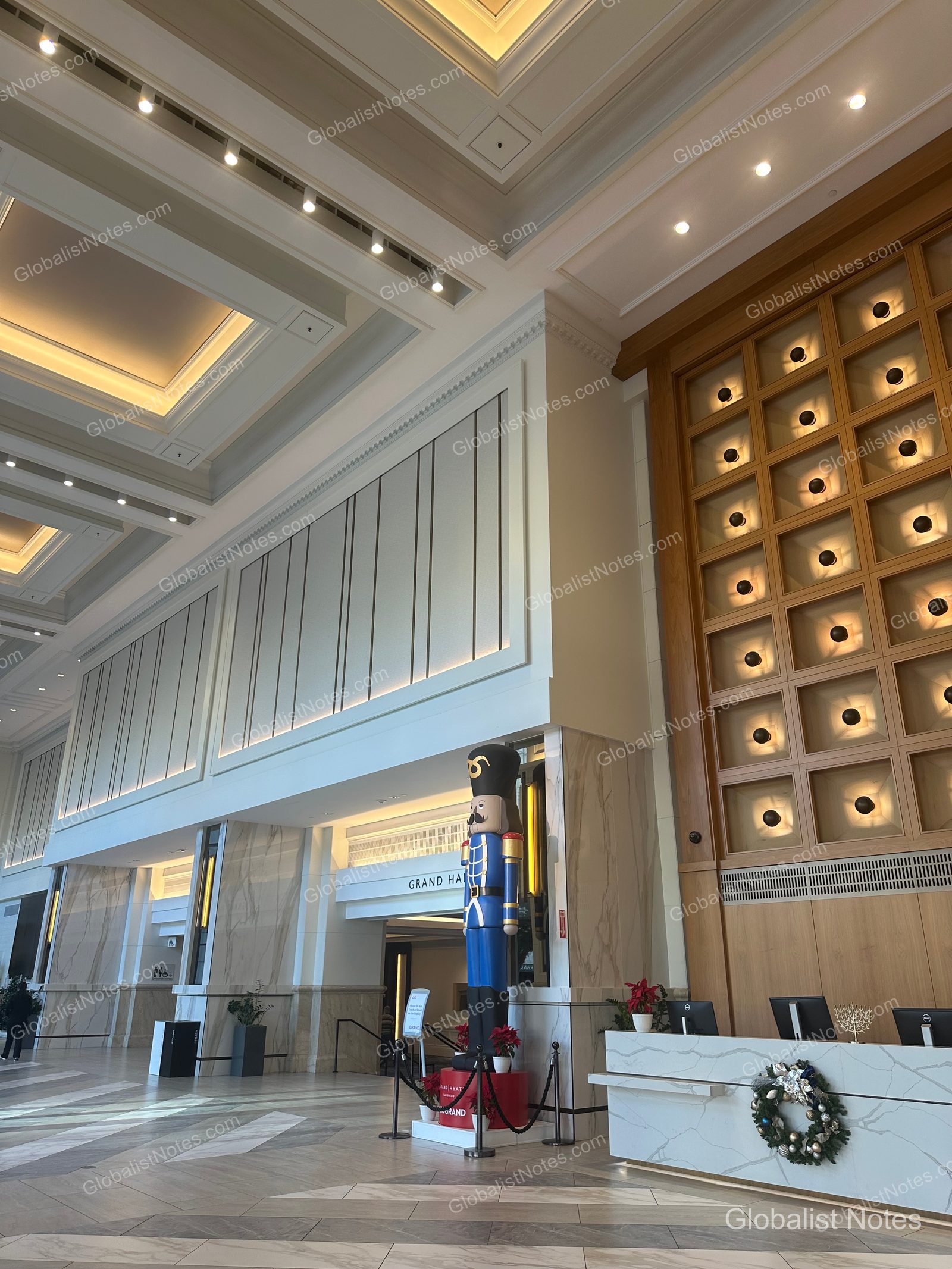 Manchester Grand Hyatt San Diego 大廳全景，挑高天花板與大理石牆面相當醒目。辦理入住櫃檯旁擺放著穿著藍色制服的大型胡桃鉗人偶與花環裝飾。