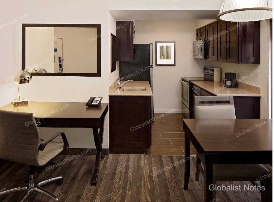 Hyatt House Scottsdale/Old Townのワンベッドルームスイート。左手にデスクとチェア、右手にはシンク、電子レンジ、収納を備えたキッチンとダイニングテーブルが配置されています。