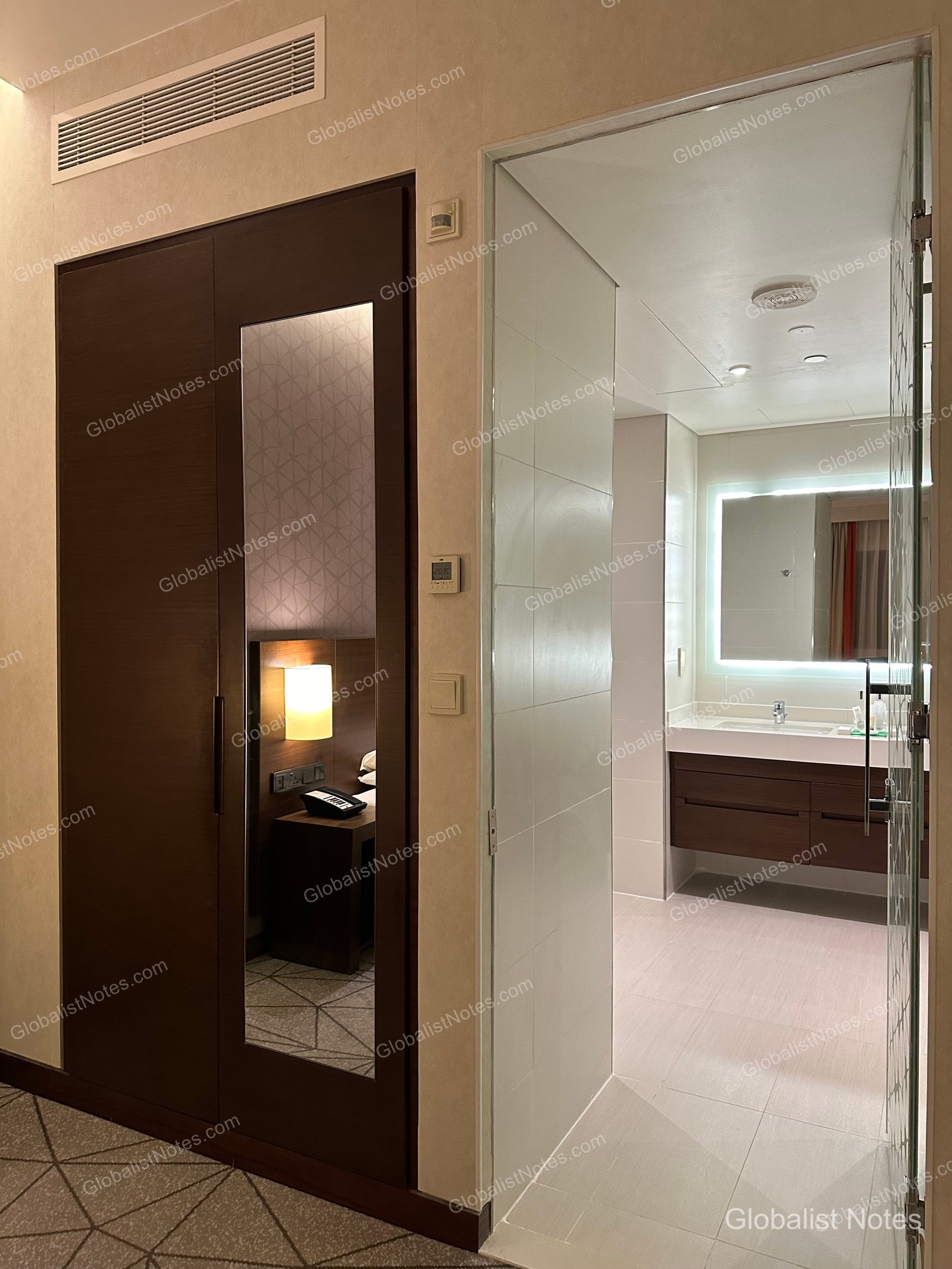 Hyatt Place Dubai Wasl District 一房套房內部，深色木質衣櫃門上的鏡面映照出床邊燈具與電話，右側為明亮的浴室入口。