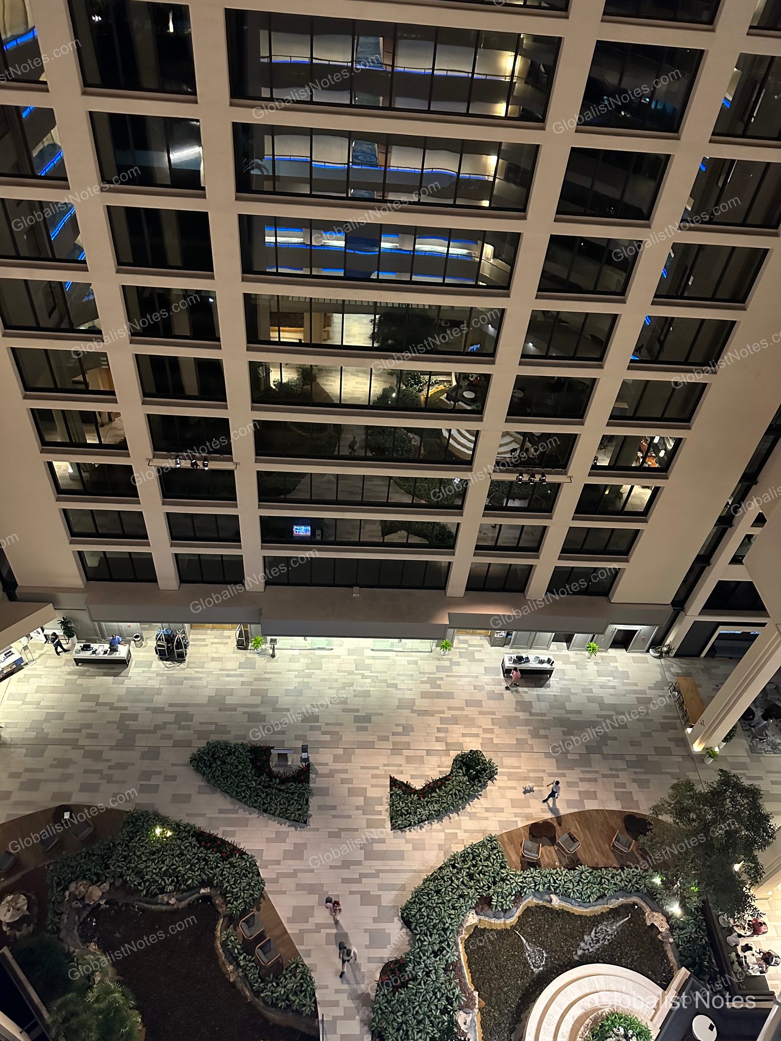 A night view of the atrium lobby at Hyatt Regency Grand Cypress in Orlando from a high floor, featuring the grid-patterned guest corridors, stone flooring, landscaped garden, and a small fountain illuminated by evening lights.