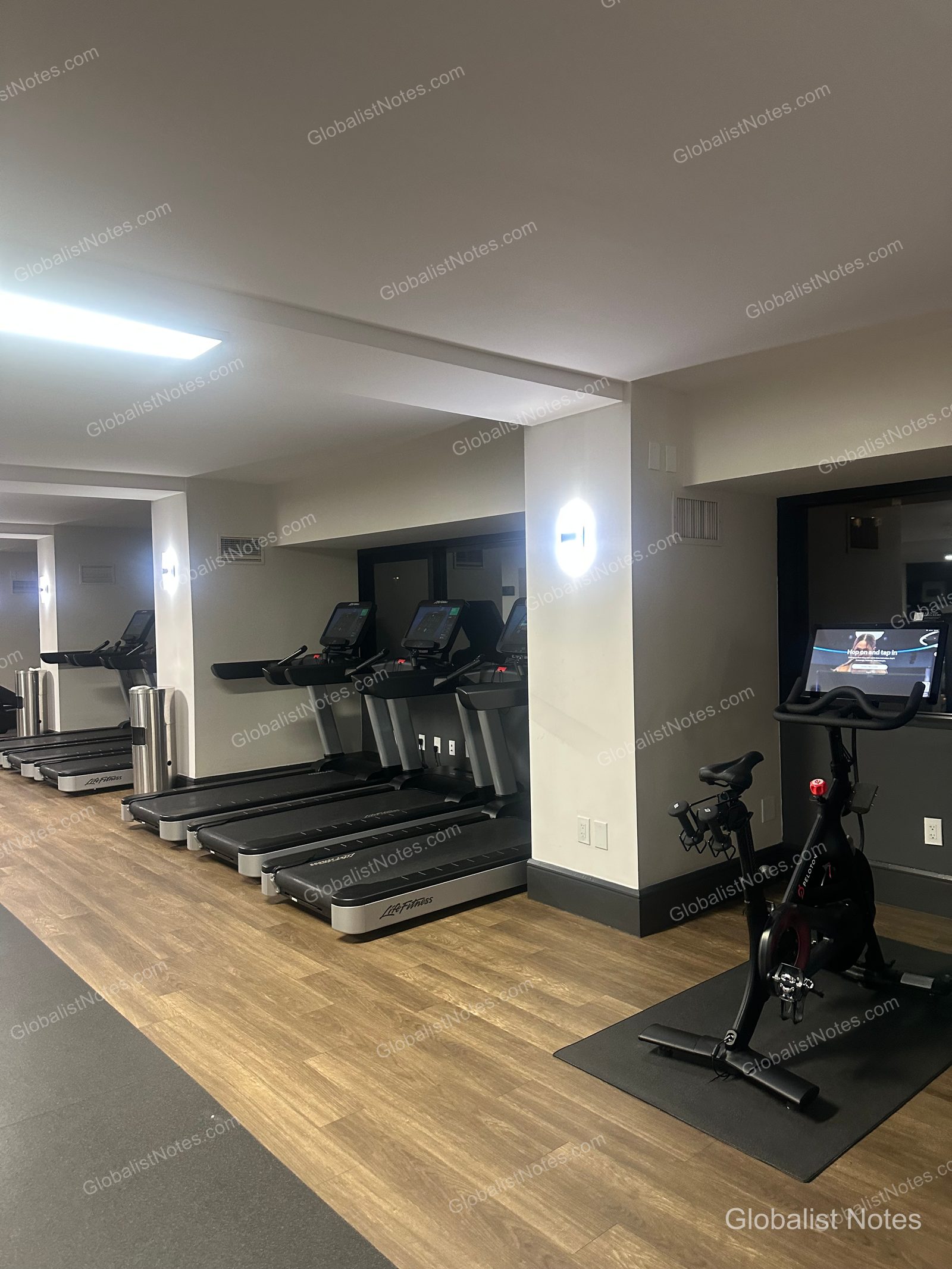 Hyatt Regency Irvine 健身中心內部，木質地板上整齊排列著多台 Life Fitness 跑步機與 Peloton 飛輪，牆面燈光營造出簡潔沉穩的氛圍。