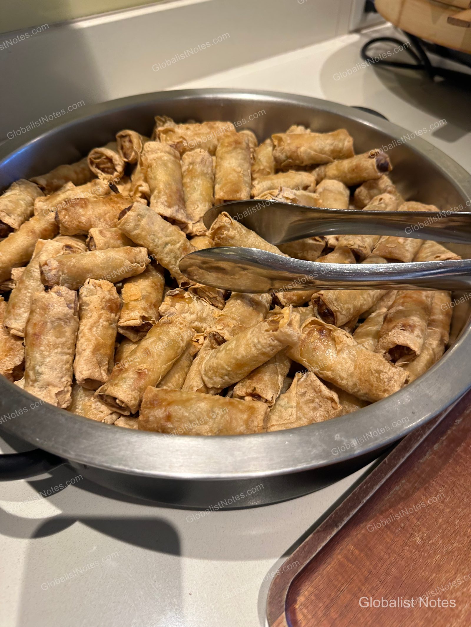 A silver circular tray at the Hyatt Regency Maui Resort and Spa breakfast buffet filled with golden-brown fried spring rolls, accompanied by metal tongs for serving.