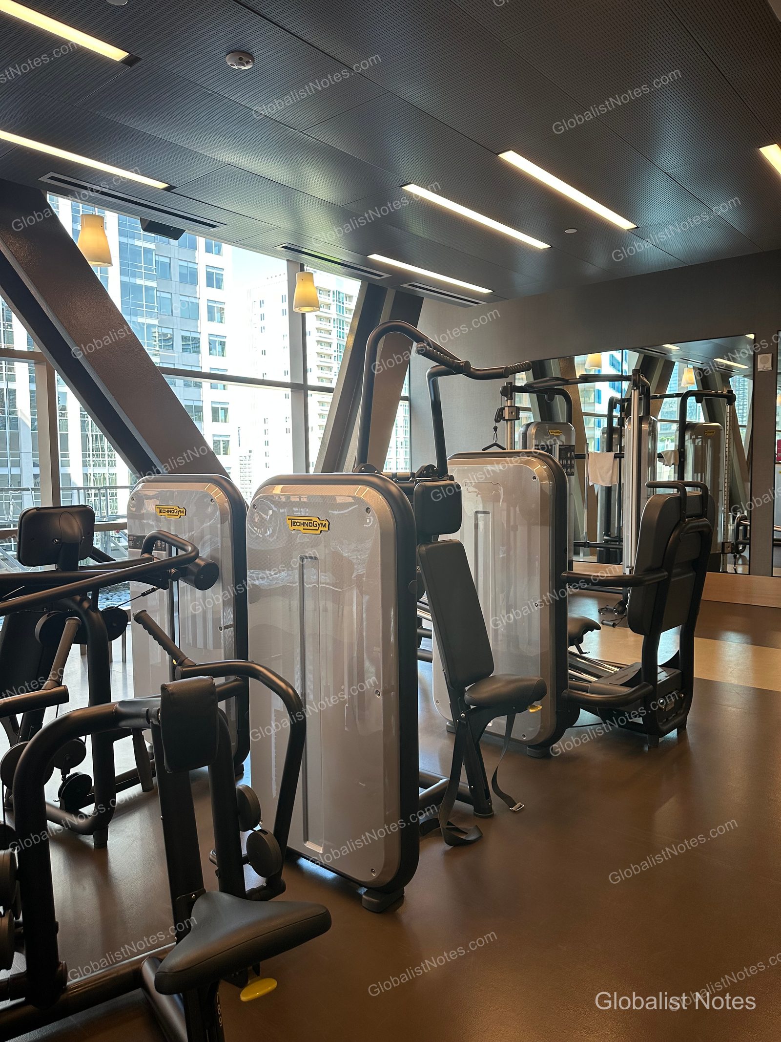 Inside the fitness center at Hyatt Regency Seattle, featuring rows of Technogym strength training equipment in a bright, modern space with floor-to-ceiling windows overlooking the Seattle city skyline.