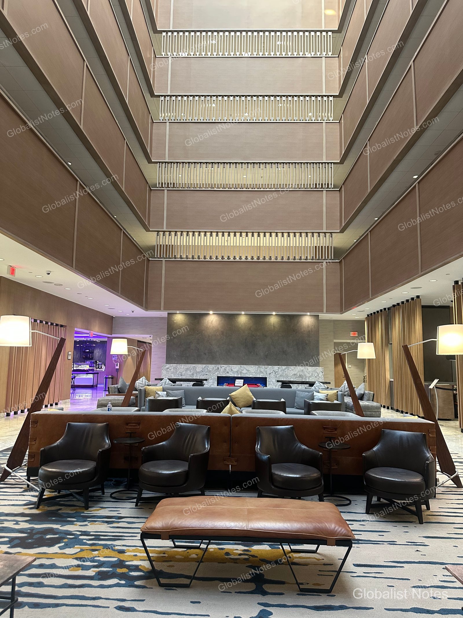 Hyatt Regency Newport Beach West 大廳全景，挑高天花板營造開闊感。中央為皮質扶手椅與沙發休憩區，後方設有大理石壁爐與幾何圖案地毯。