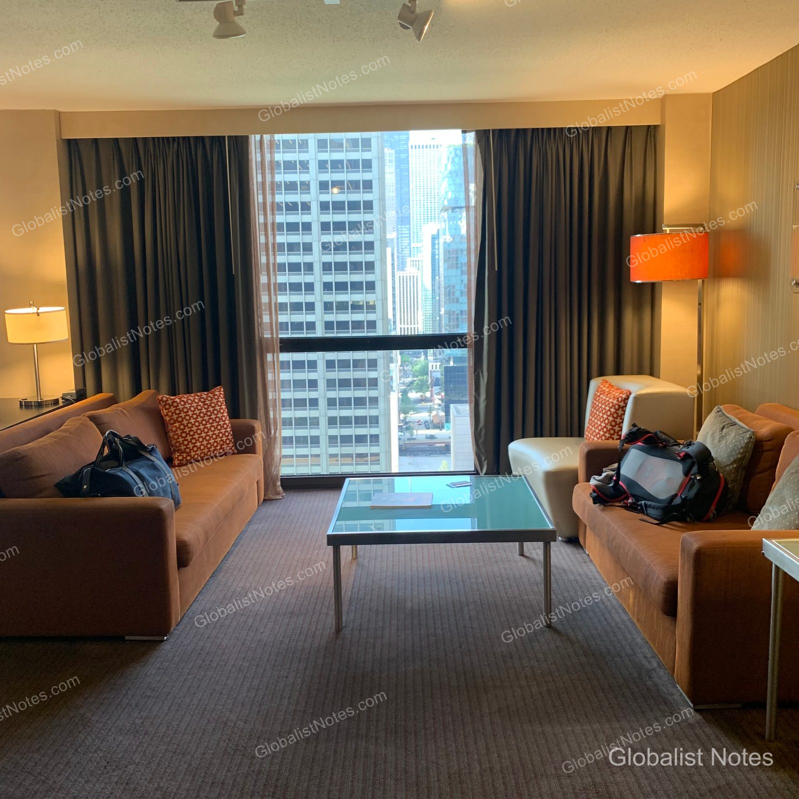 Hyatt Regency Chicagoのジュニアスイートのリビングエリア。向かい合わせに配置された2つのソファとガラステーブルが置かれ、窓の外にはシカゴのビル群が広がっています。