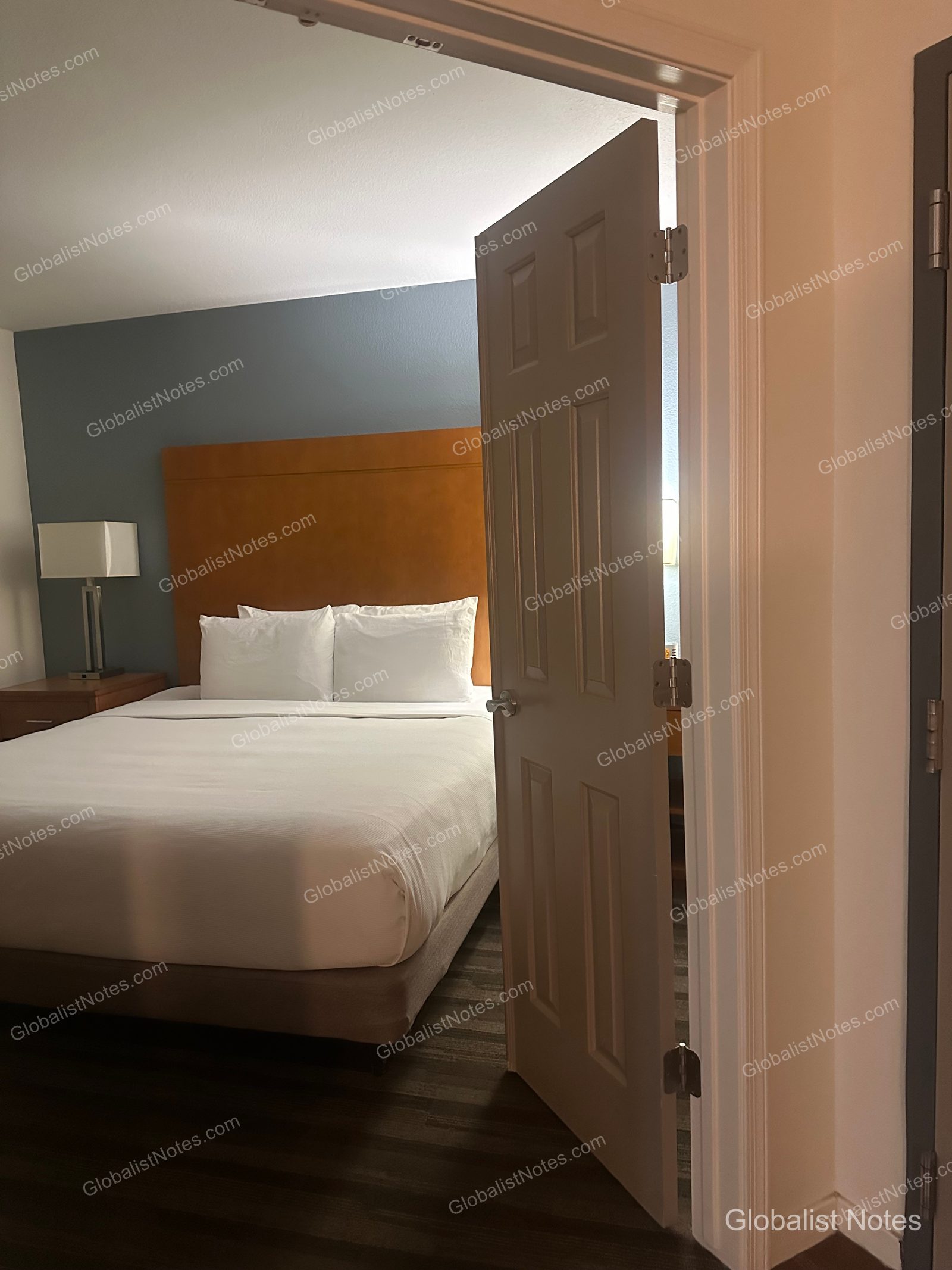 Hyatt House Scottsdale/Old Townの1ベッドルームスイート。ドア越しにベッド、ブラウンのヘッドボード、照明付きのナイトスタンドが見える。