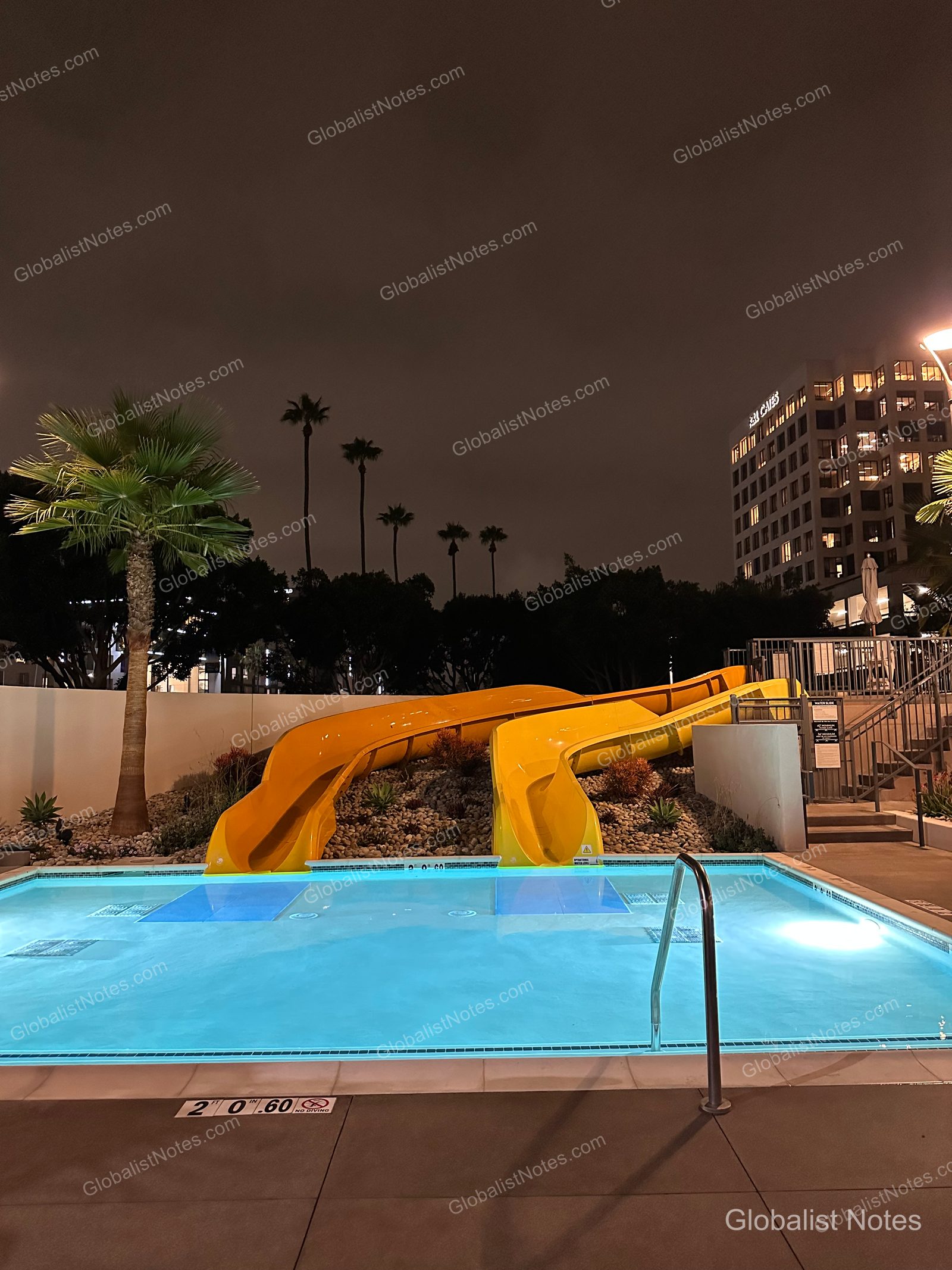 夜間點燈後的 Hyatt Regency Irvine 戶外泳池，後方設有兩座黃色滑水道，背景為棕櫚樹與飯店建築。