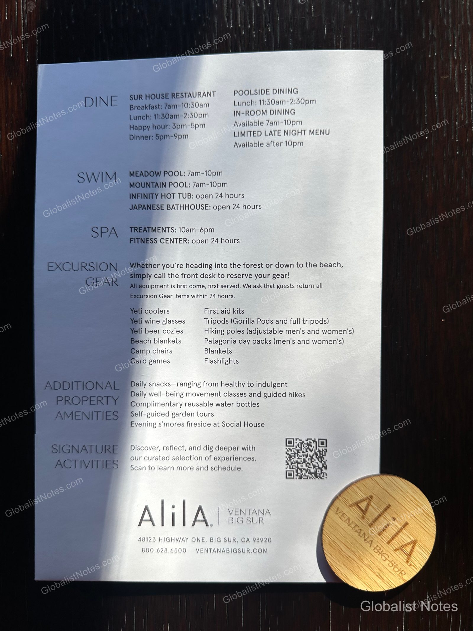 An information sheet for Alila Ventana Big Sur listing facility operating hours and available outdoor activity equipment. It includes details on dining, the pool, spa, excursions, and additional amenities, with a wooden room key card featuring the hotel logo placed at the bottom.