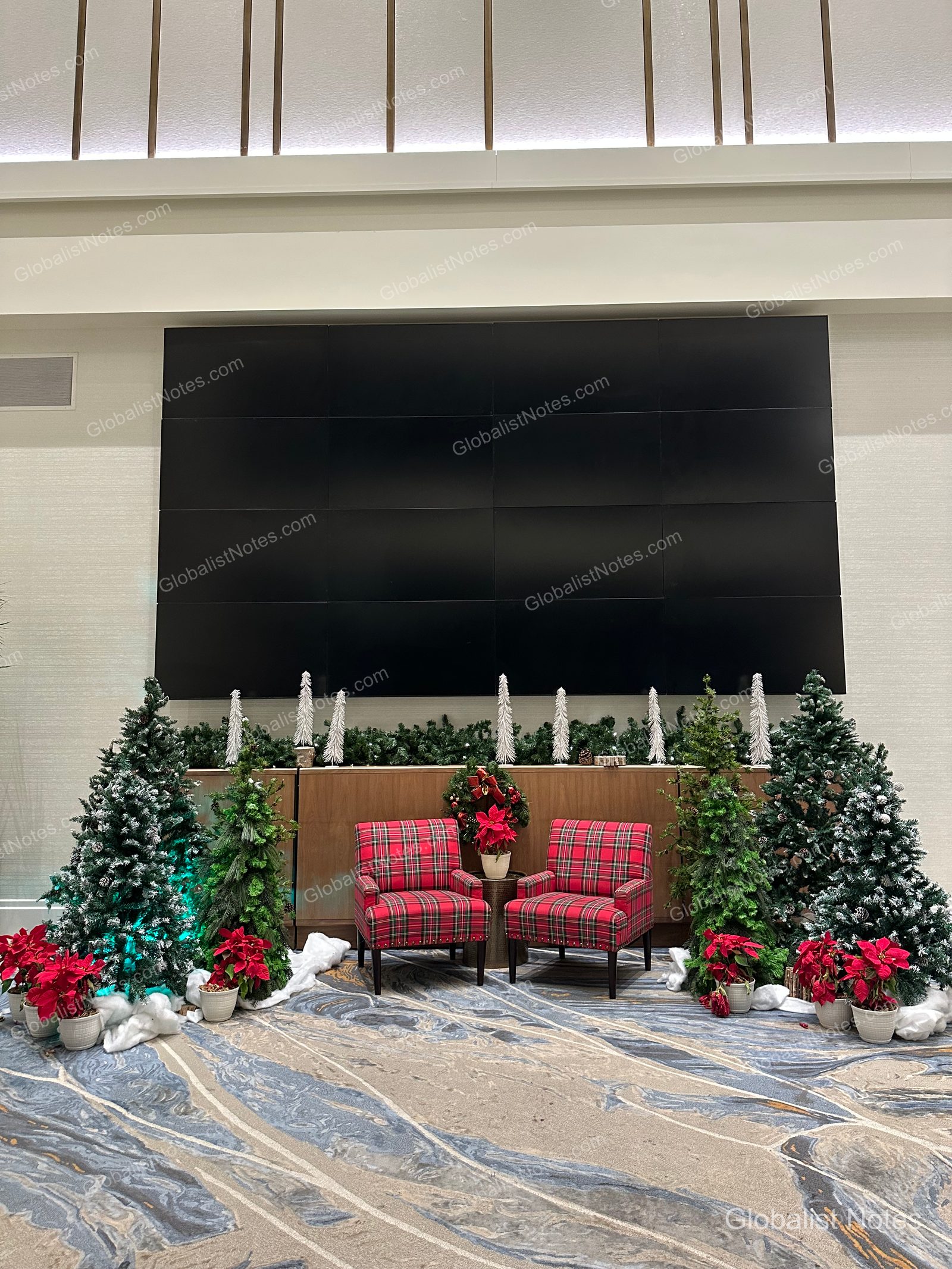 Manchester Grand Hyatt 大廳的聖誕裝飾，中央擺放兩張紅色格紋椅，周圍點綴著小型聖誕樹與聖誕紅，充滿年終節慶氛圍。