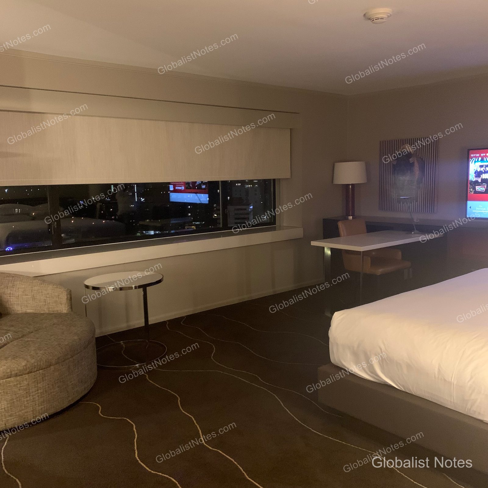 Grand Hyatt Denverの1キングベッド コーナー客室。右手にキングベッドと壁掛けテレビ、左手にアームチェアとテーブルが配されている。窓からはデンバー市街の夜景が広がり、落ち着いたトーンでまとめられたインテリア。